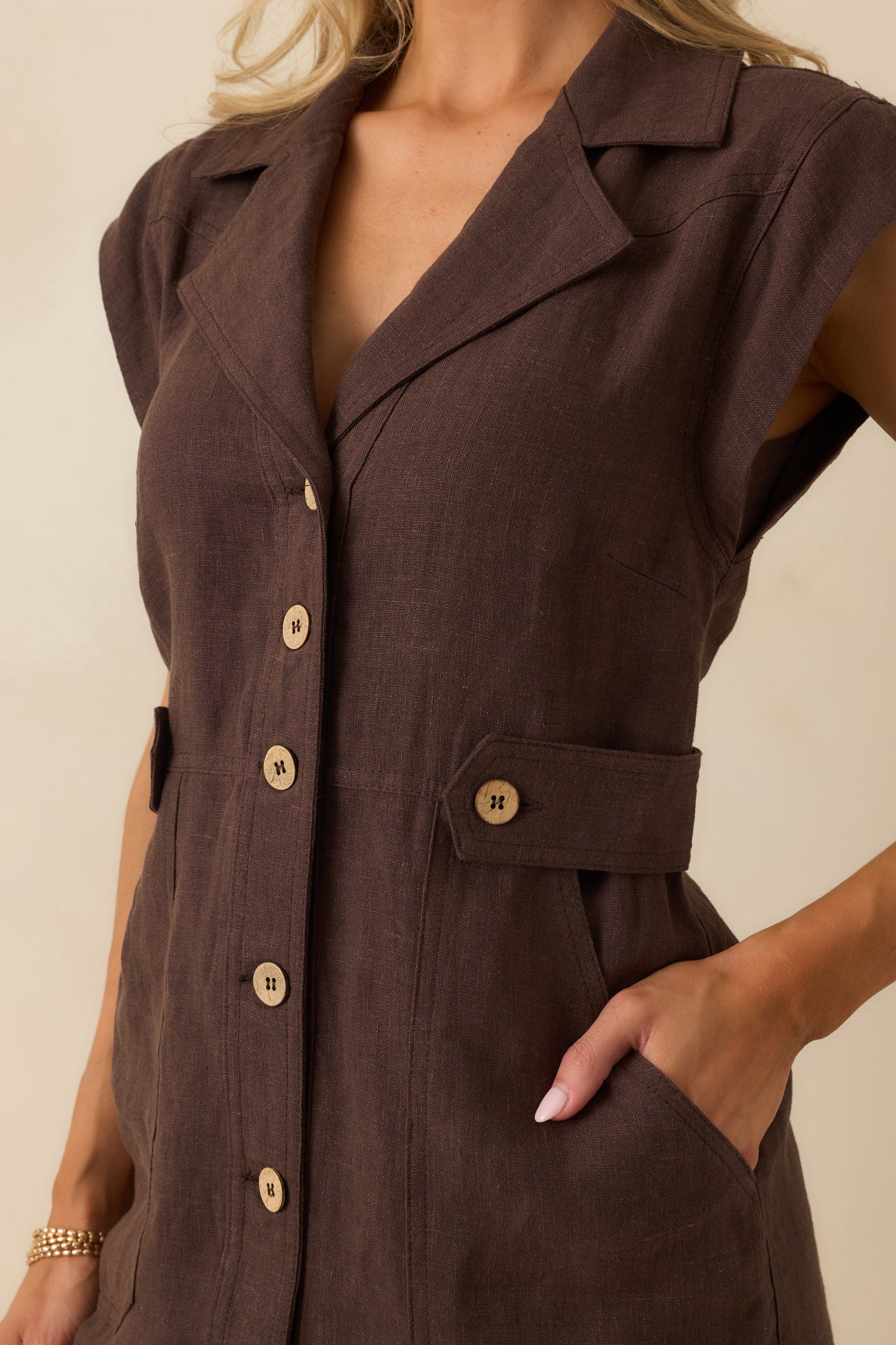 Detailed shot of brown linen fabric, notched lapel collar, wooden buttons, and front patch pockets.