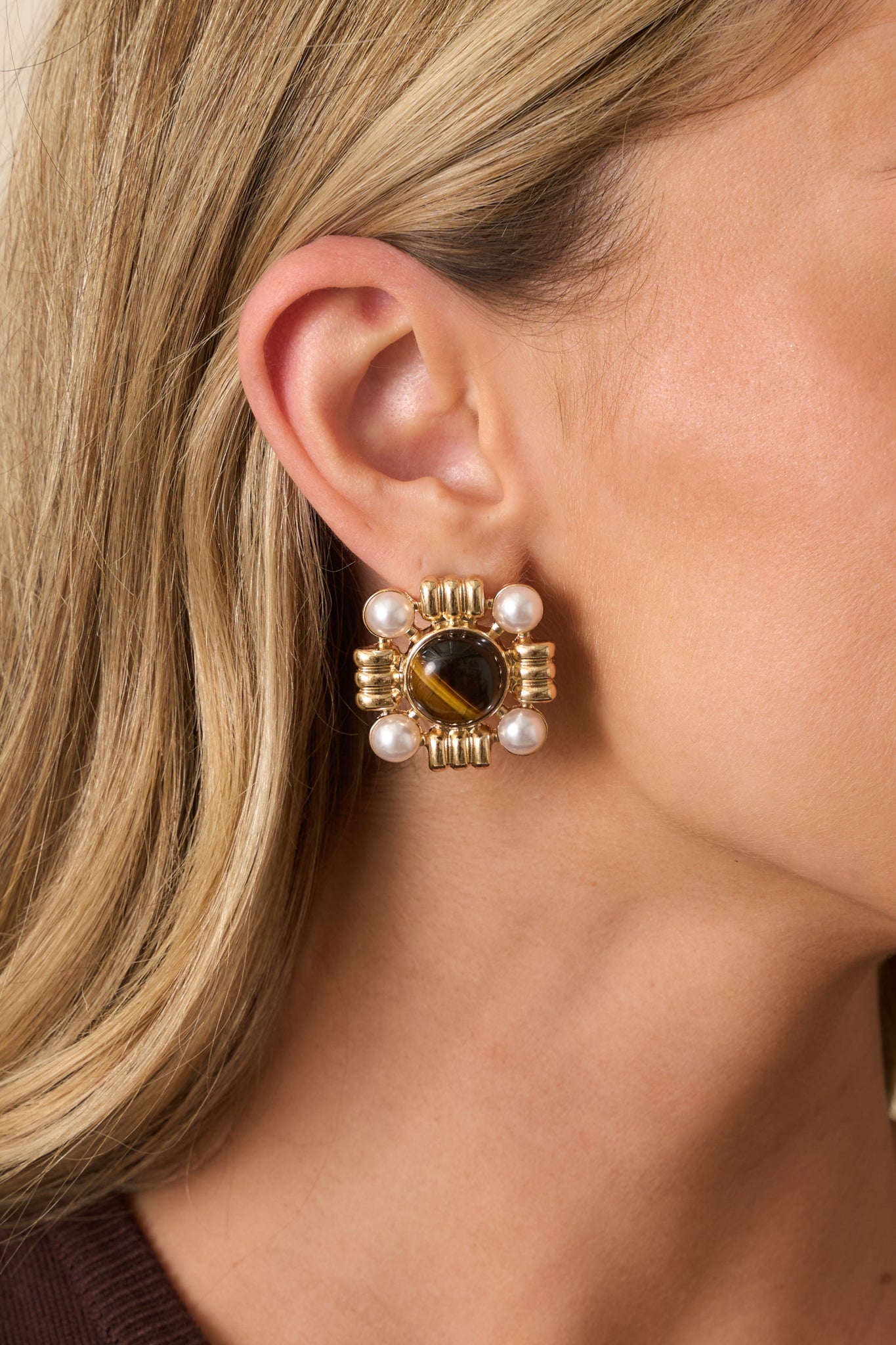 A close-up of one earring showing the brown marbled round center stone, four ivory faux pearls in the corners, and textured gold framework with a post back.