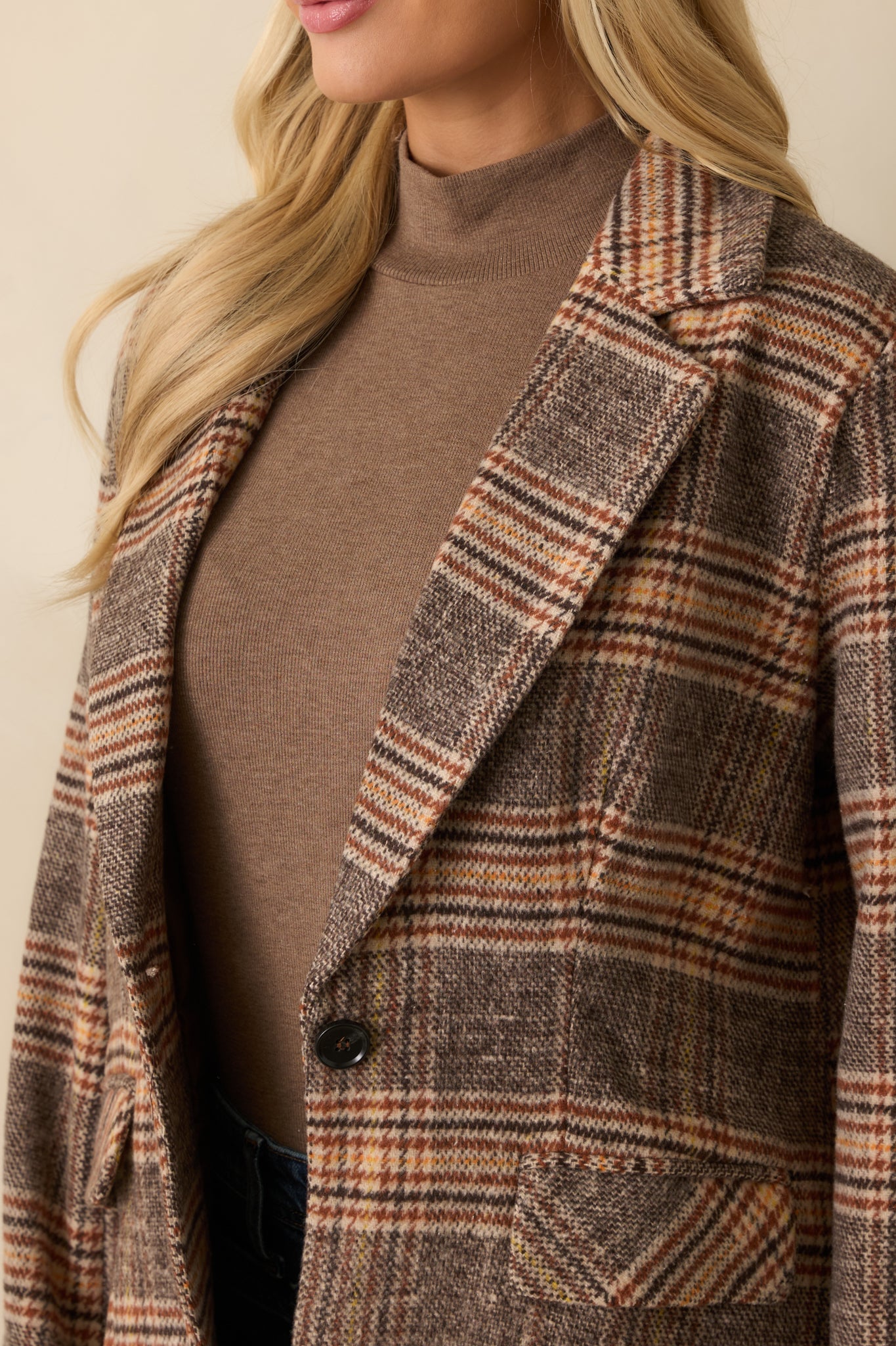 Detailed look at the plaid pattern, front buttons, and textured fabric of the brown overcoat.