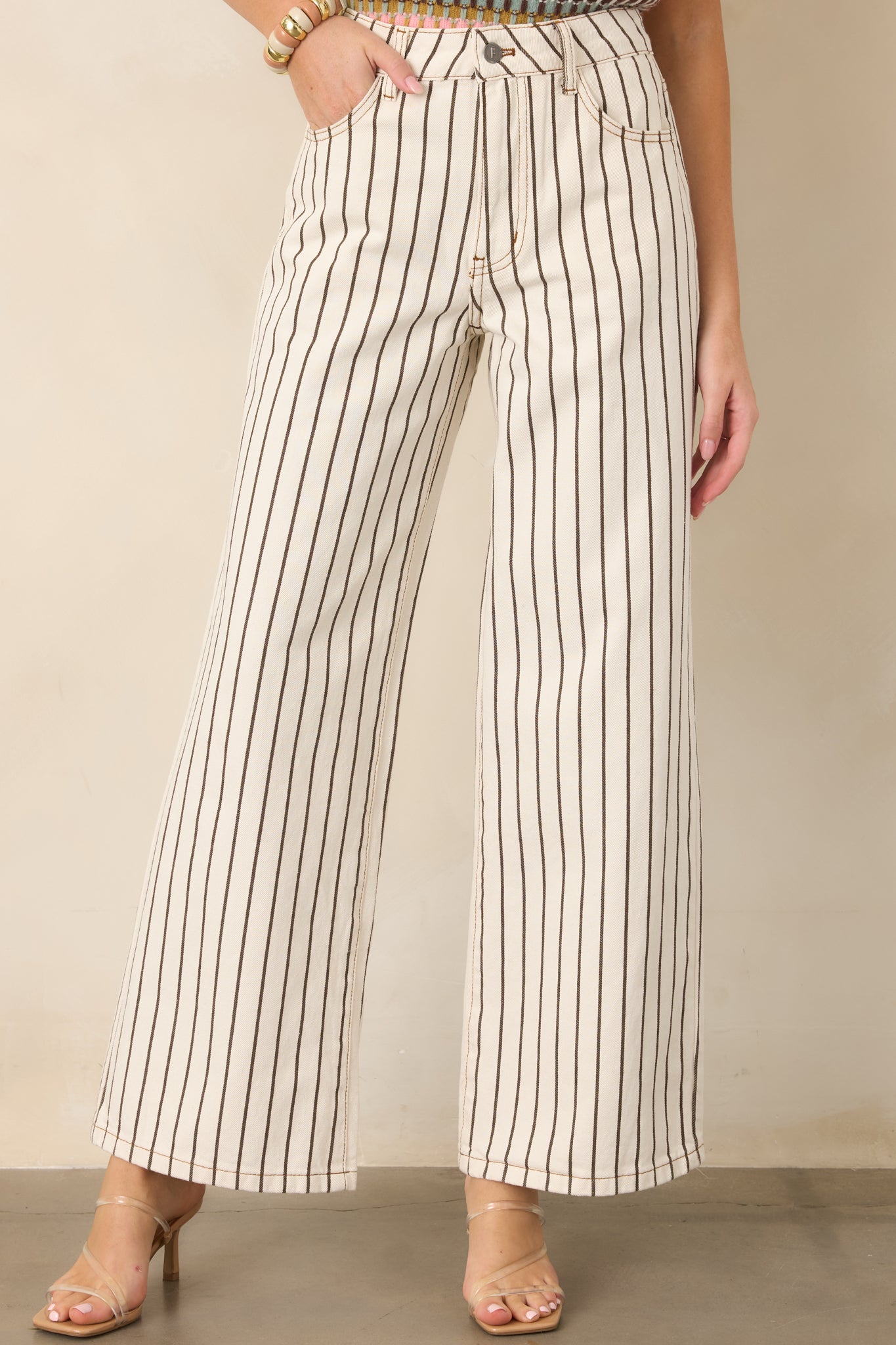 Brown pinstripes run vertically across the crisp ivory denim pants, emphasizing the tailored appearance and elongated wide-leg shape.