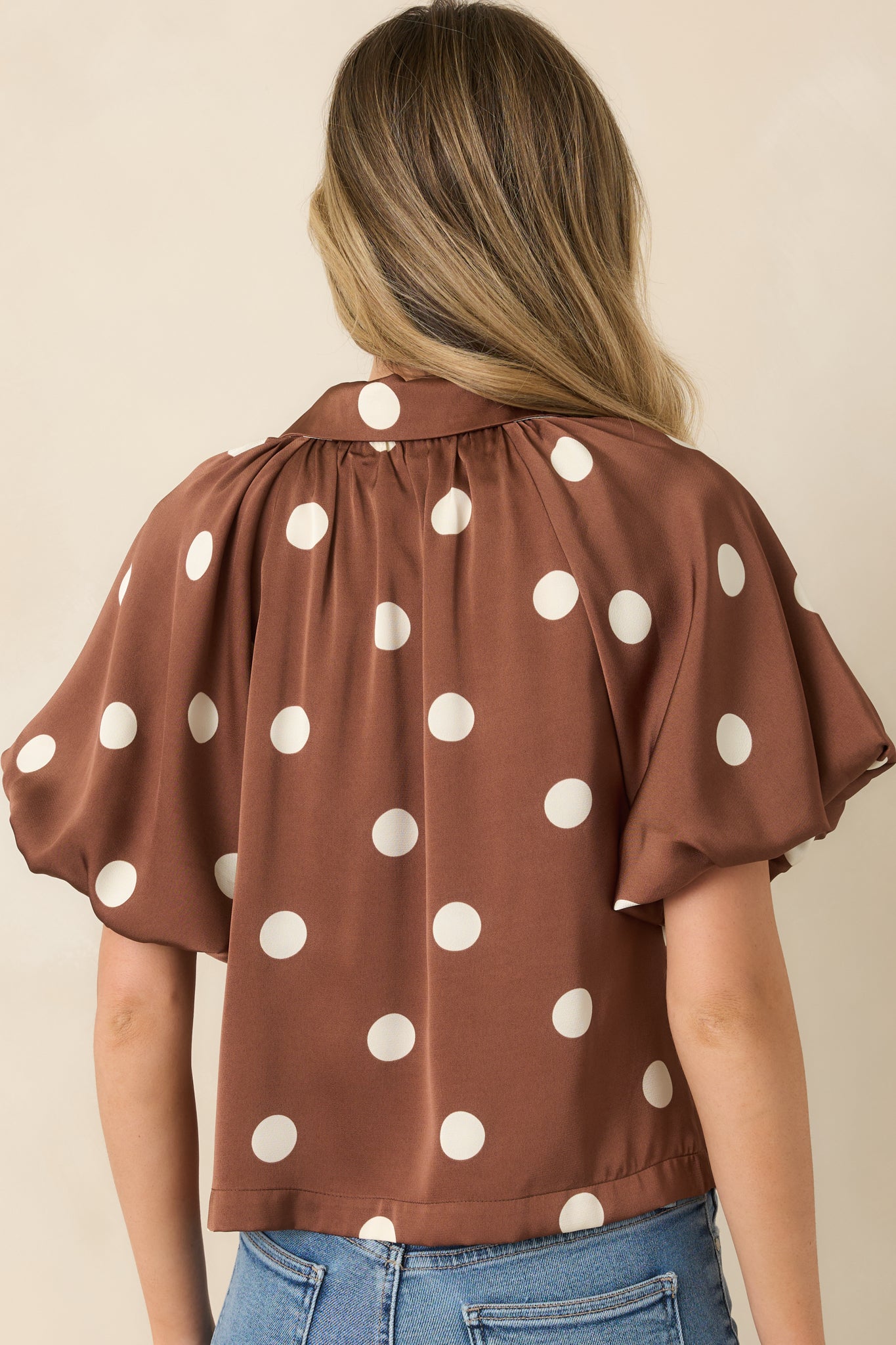 Back view of the brown polka dot blouse featuring gathered shoulder detailing, puff sleeves, and a smooth draped finish.