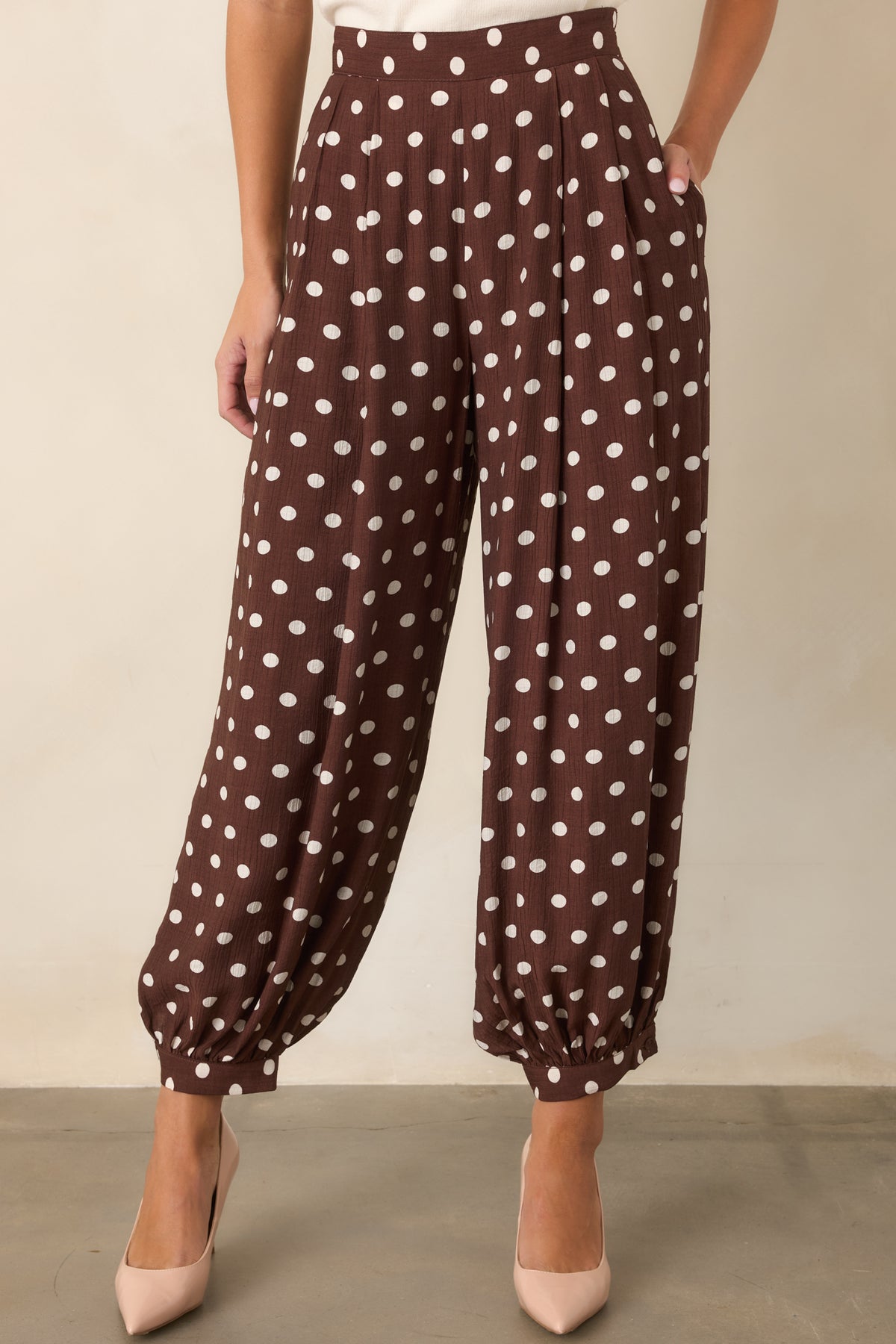Brown pants showcasing ivory polka dots, a high-rise waistband, and structured front pleats.
