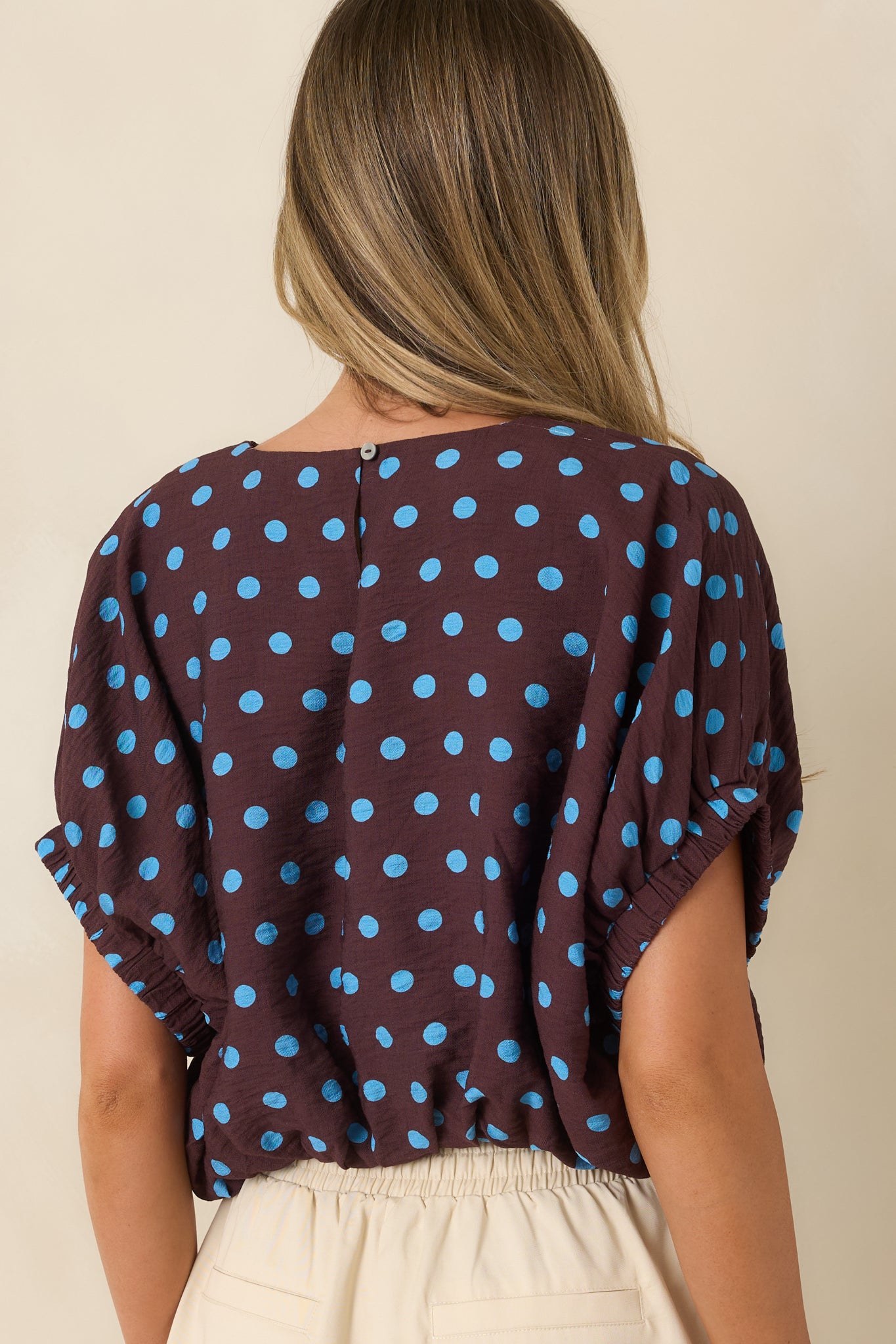 Rear view of the brown polka dot top featuring a relaxed silhouette and smooth draped fabric.