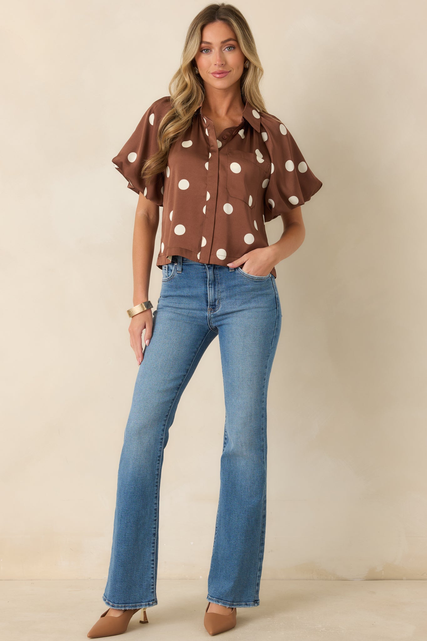 Polka dot blouse featuring a rich brown background, smooth woven fabric, statement sleeves, and a polished collared neckline.