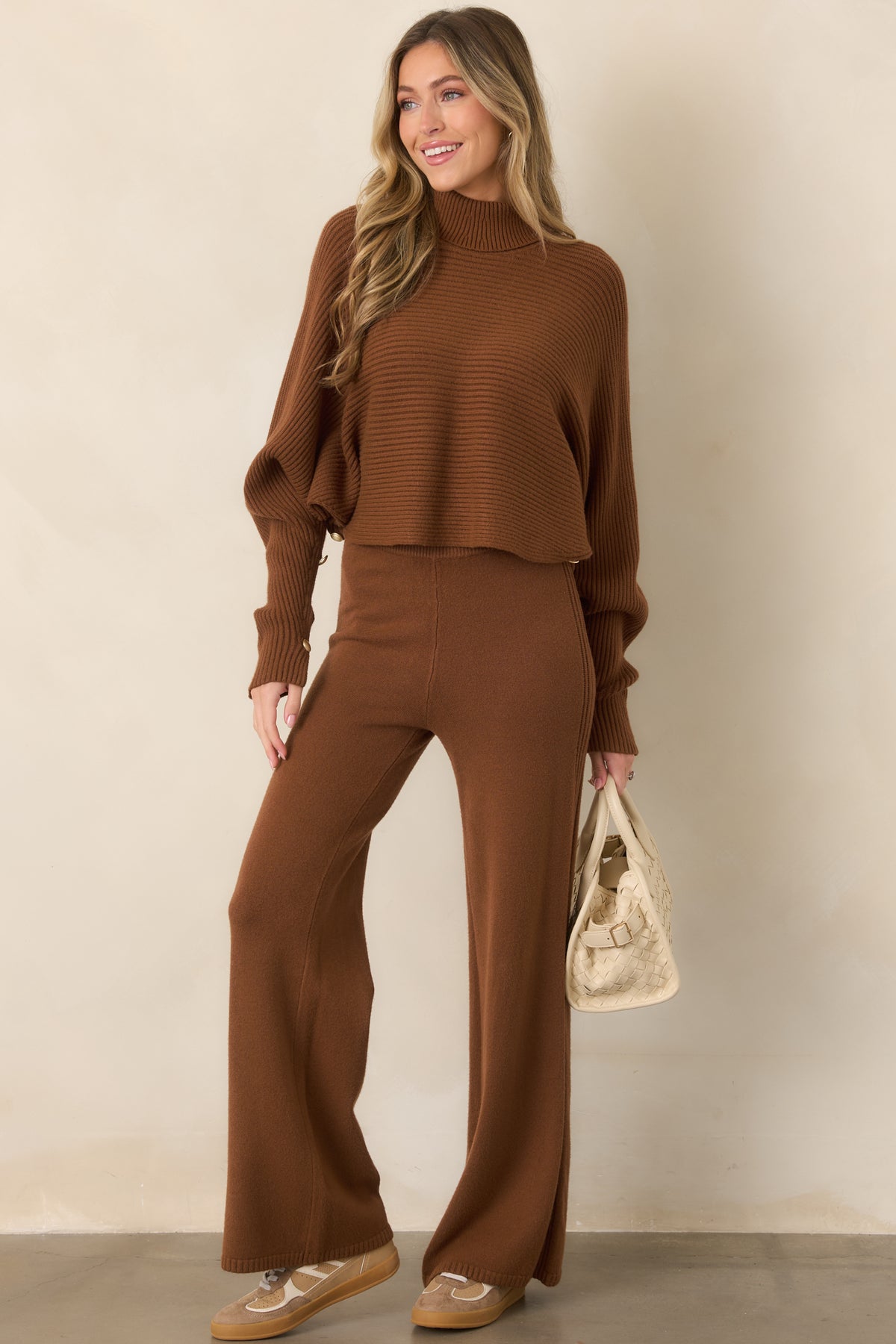 Brown ribbed pullover sweater with a high turtleneck, generously draped batwing sleeves, button-accented cuffs, and a softly cropped hem.