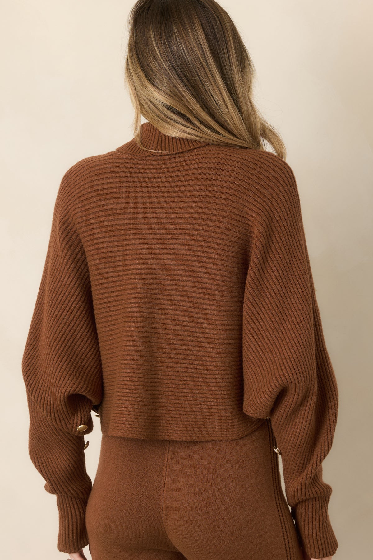 Rear view of the brown ribbed sweater showcasing the relaxed batwing silhouette, turtleneck collar, cropped hem, and softly draped back.