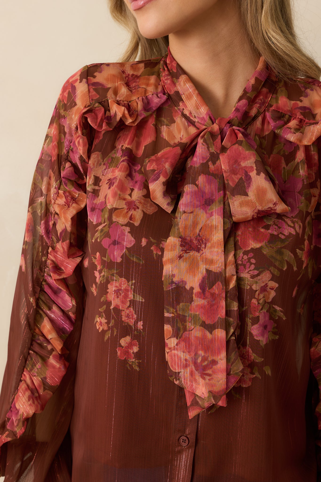 Tight shot of brown sheer fabric showing multi floral print, ruffle trim, and smocked sleeve cuffs.