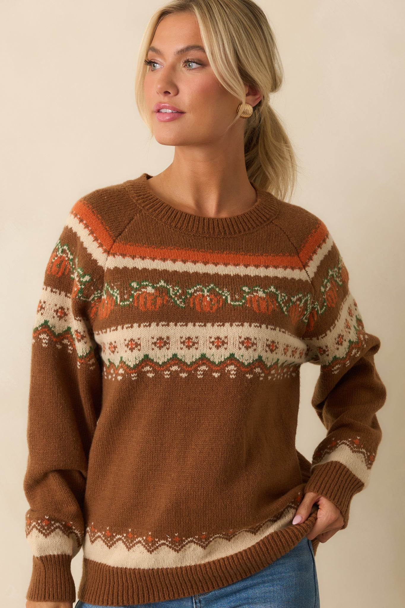 Midsection crop of brown sweater showing relaxed fit and vibrant pumpkin and floral knit design.