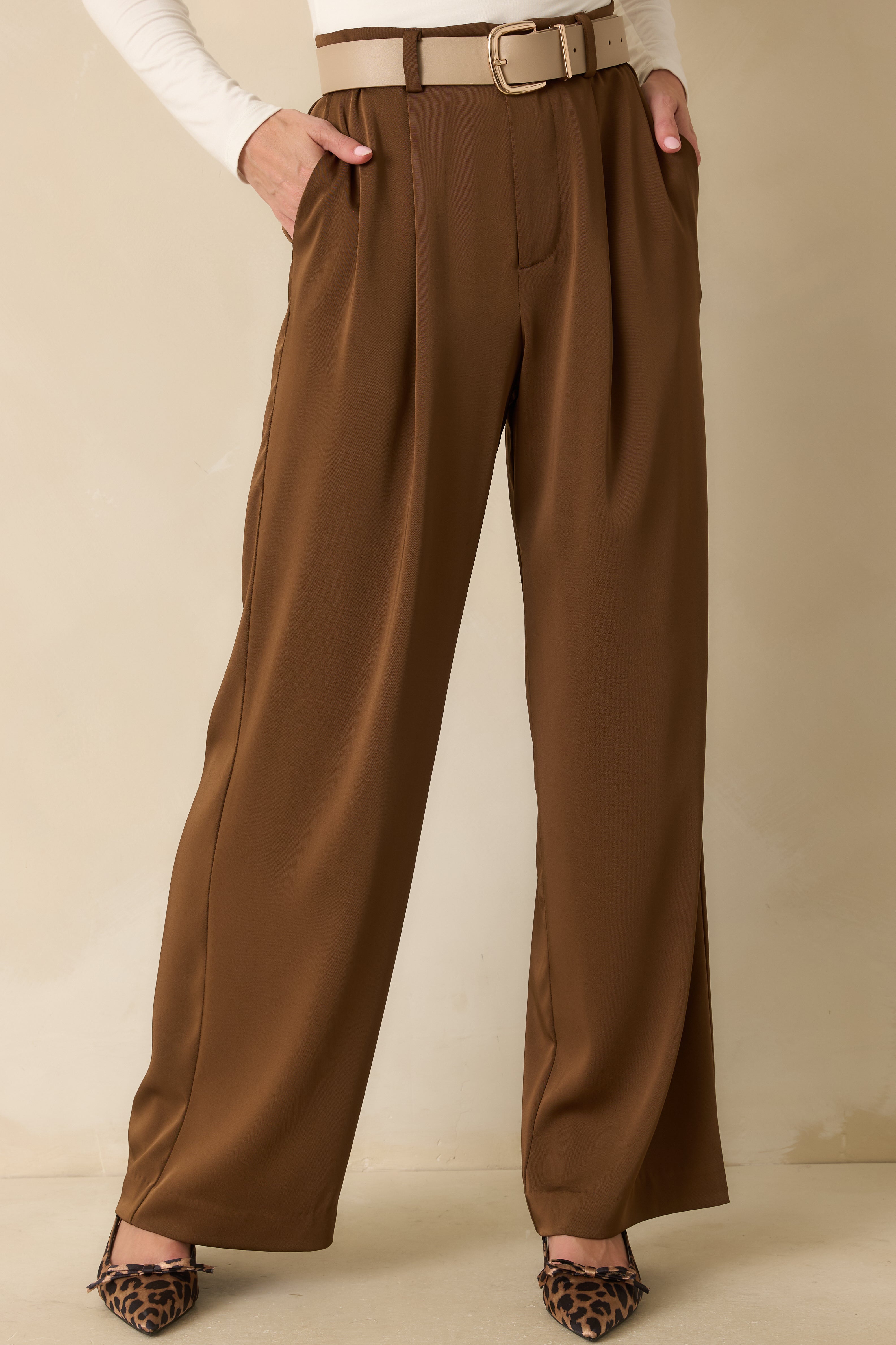 Close crop highlighting the pleated front and functional side pockets of the brown trousers.