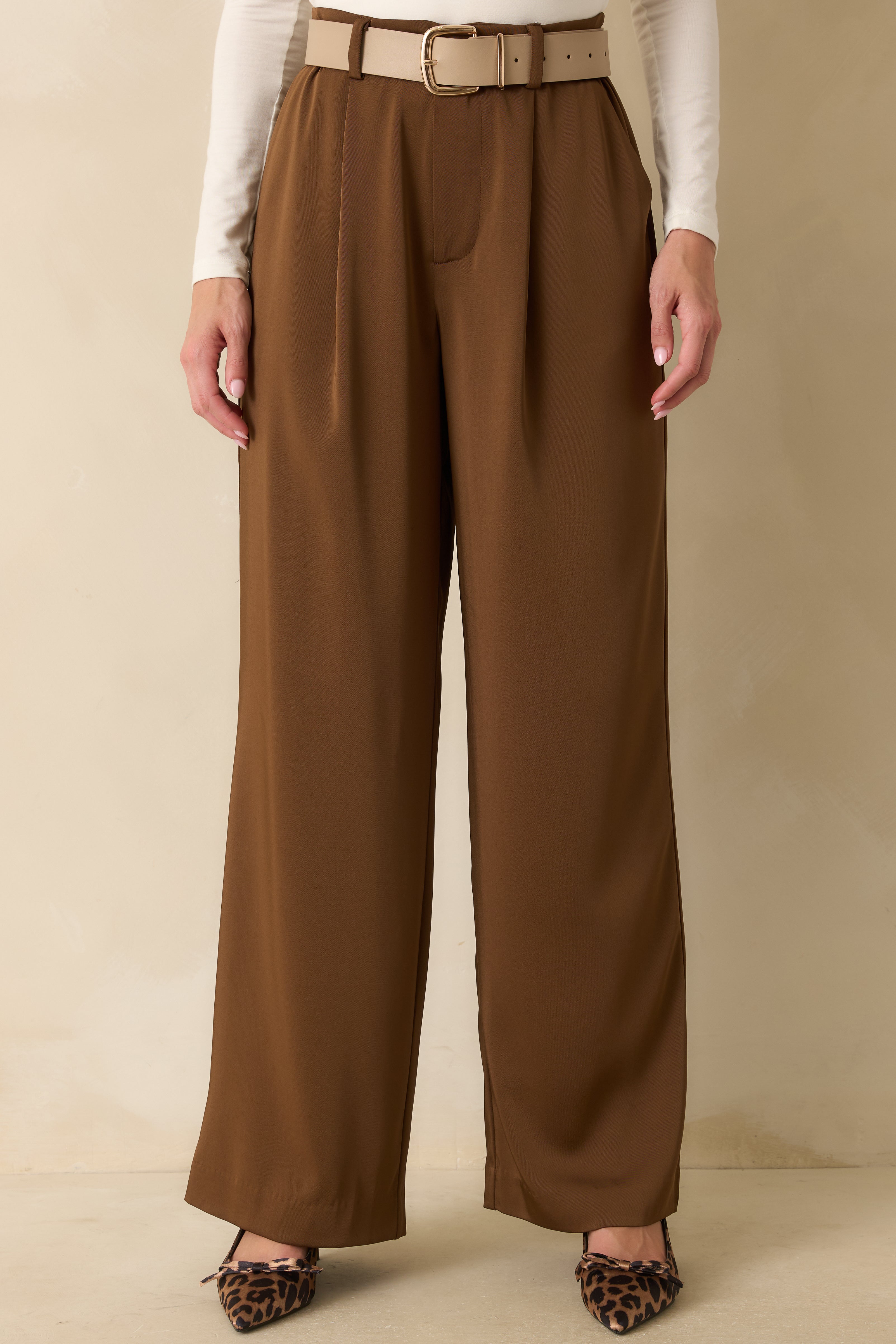 Close crop highlighting the pleated front and functional side pockets of the brown trousers.