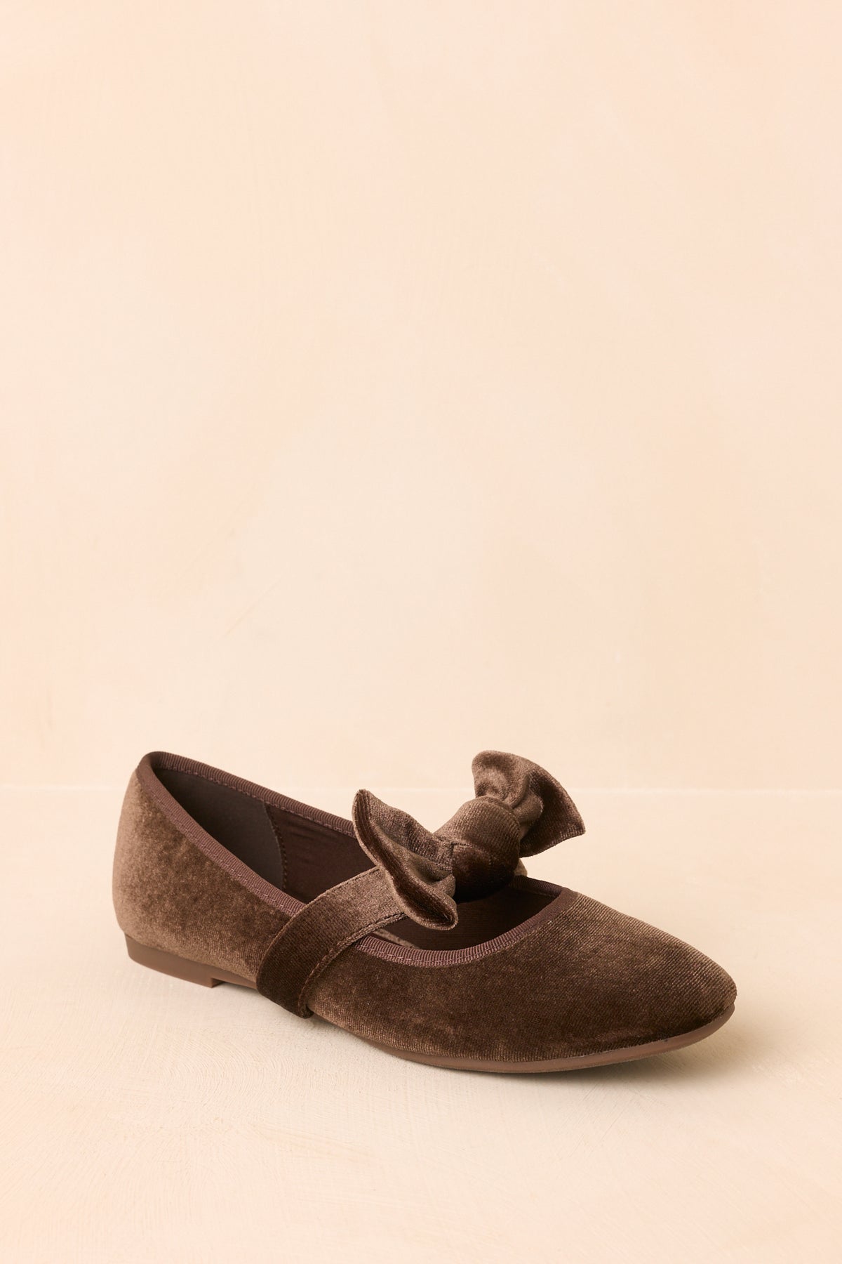 Brown velvet flats shown from the side, highlighting the rounded toe, tonal trim, and low heel.