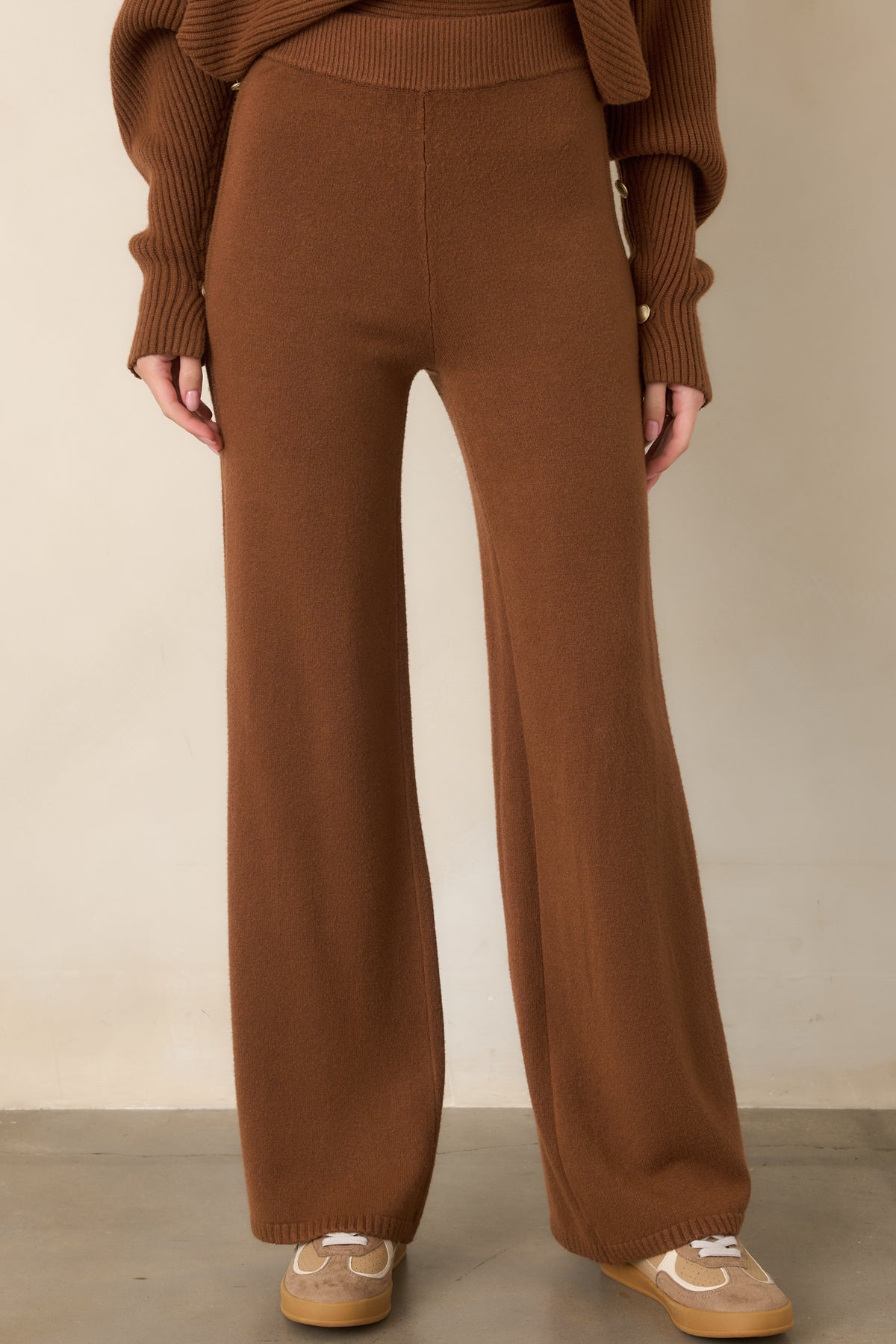 Brown wide-leg pants shown in detail with a smooth knit finish, defined side seams, and textured ribbed accents running vertically along the legs.