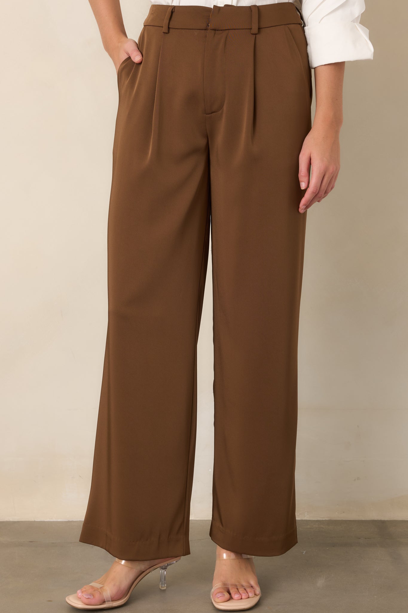 Brown wide-leg trousers highlighting the pleated waist and functional side pockets.