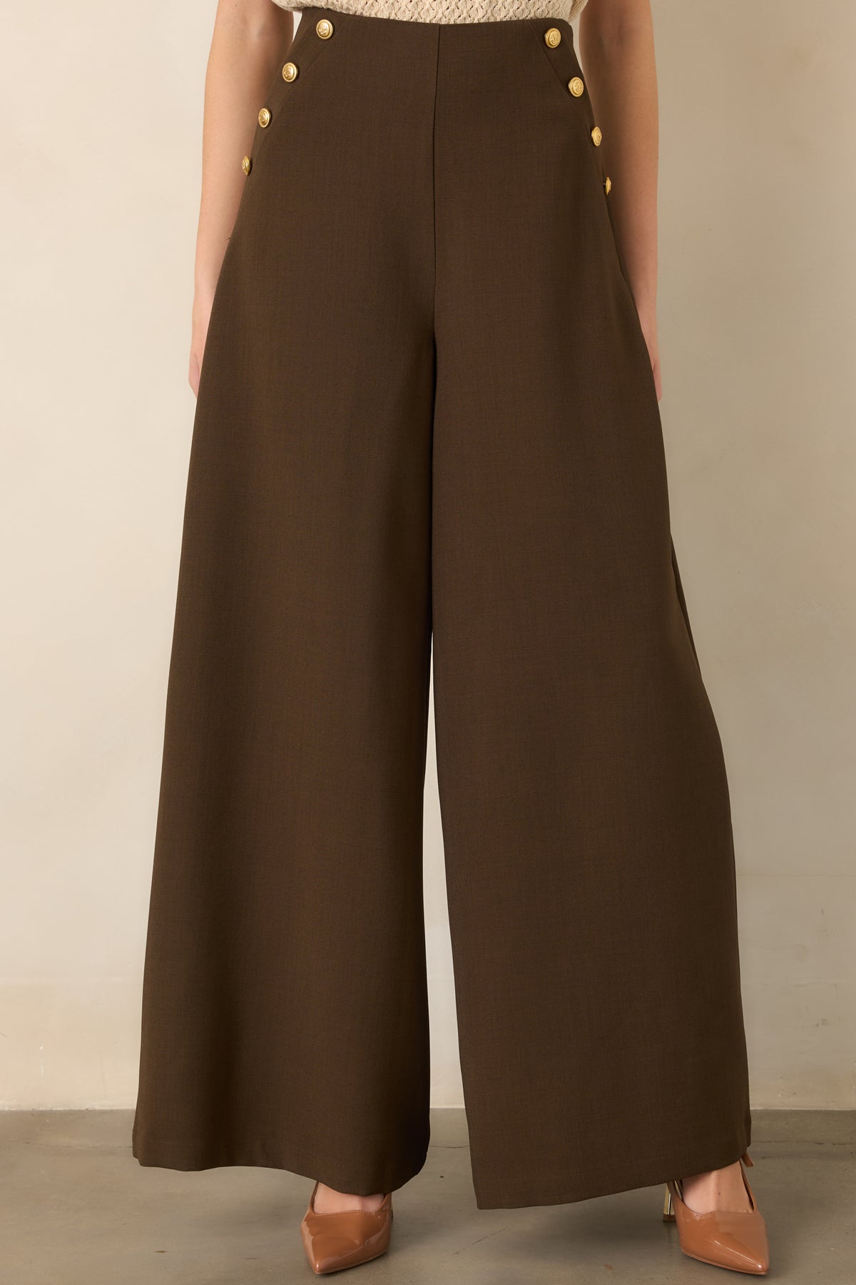 Detailed view of the brown trousers showcasing the smooth woven texture, tailored upper fit, and decorative metallic buttons.