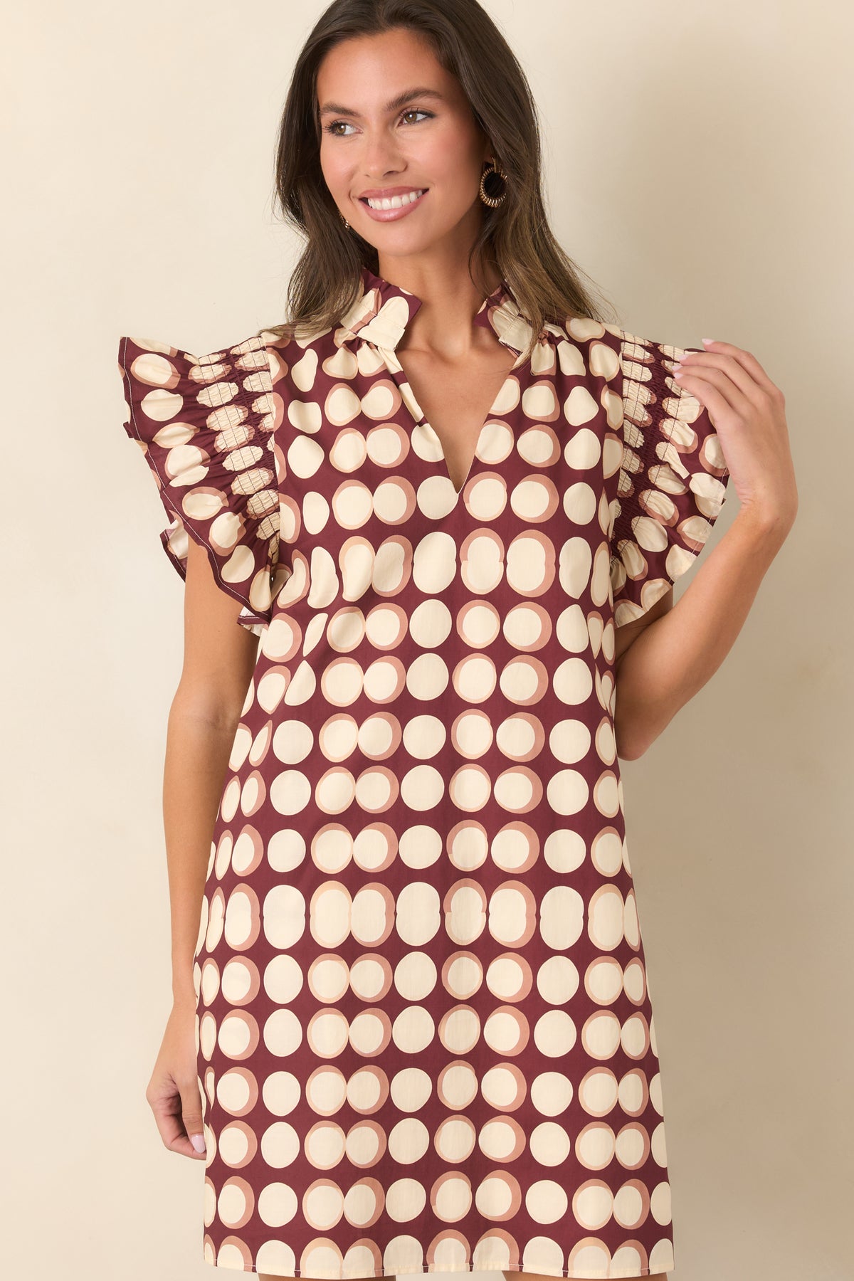 Burgundy mini dress featuring bold ivory dots, a ruffled split neckline, flutter sleeves, and a loose pull-on silhouette.