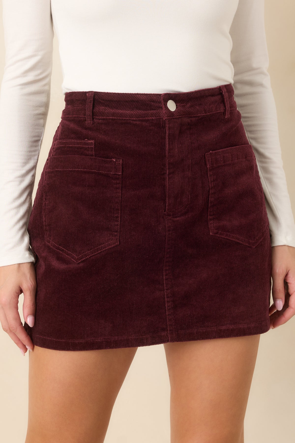 Fine burgundy corduroy ribbing and tonal stitching highlight the skirt's textured fabric and pocket construction.