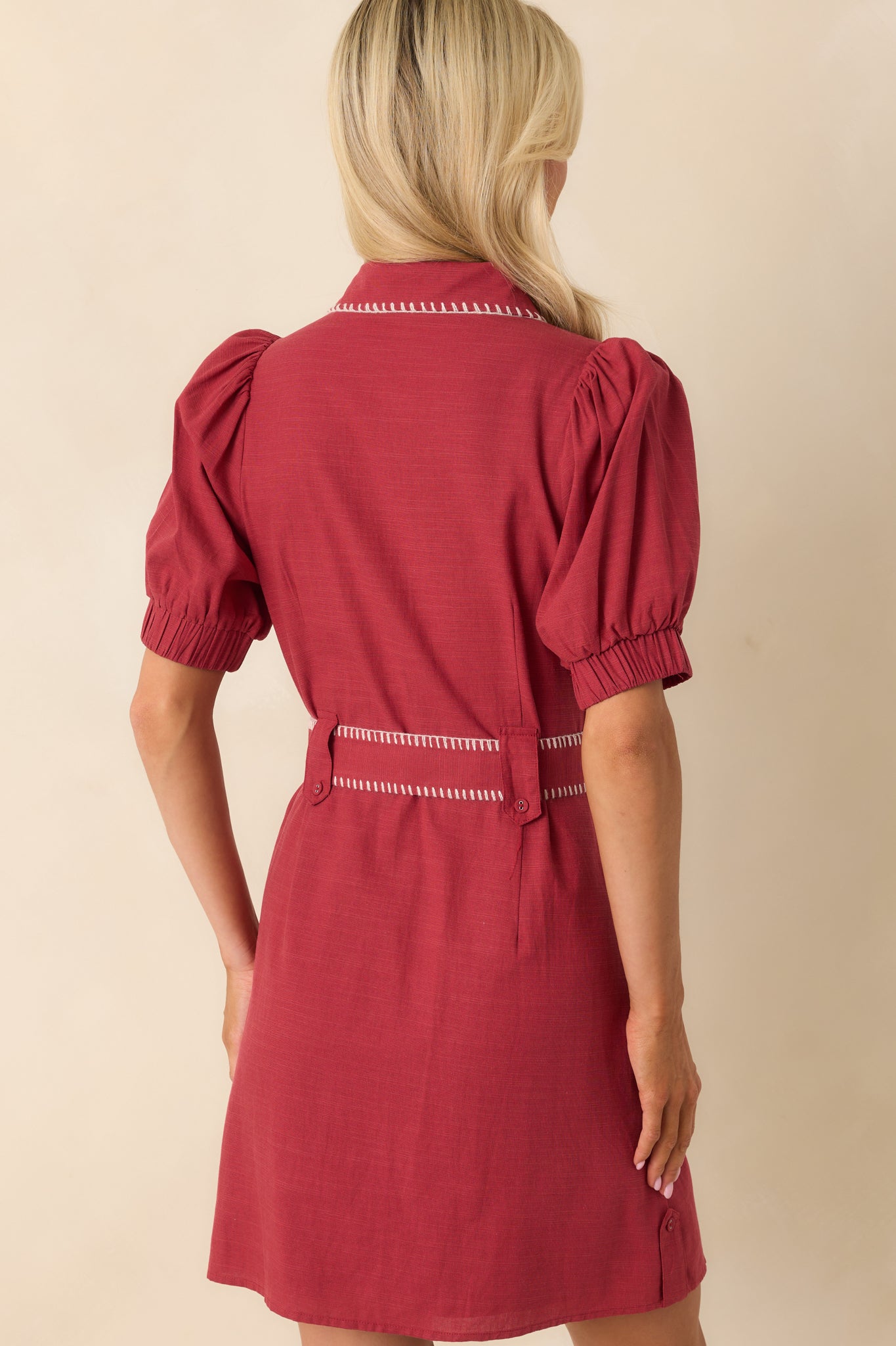 A view from behind of the burgundy mini dress, displaying the full white stitch trim along the collar, sleeves, waist, and hemline.