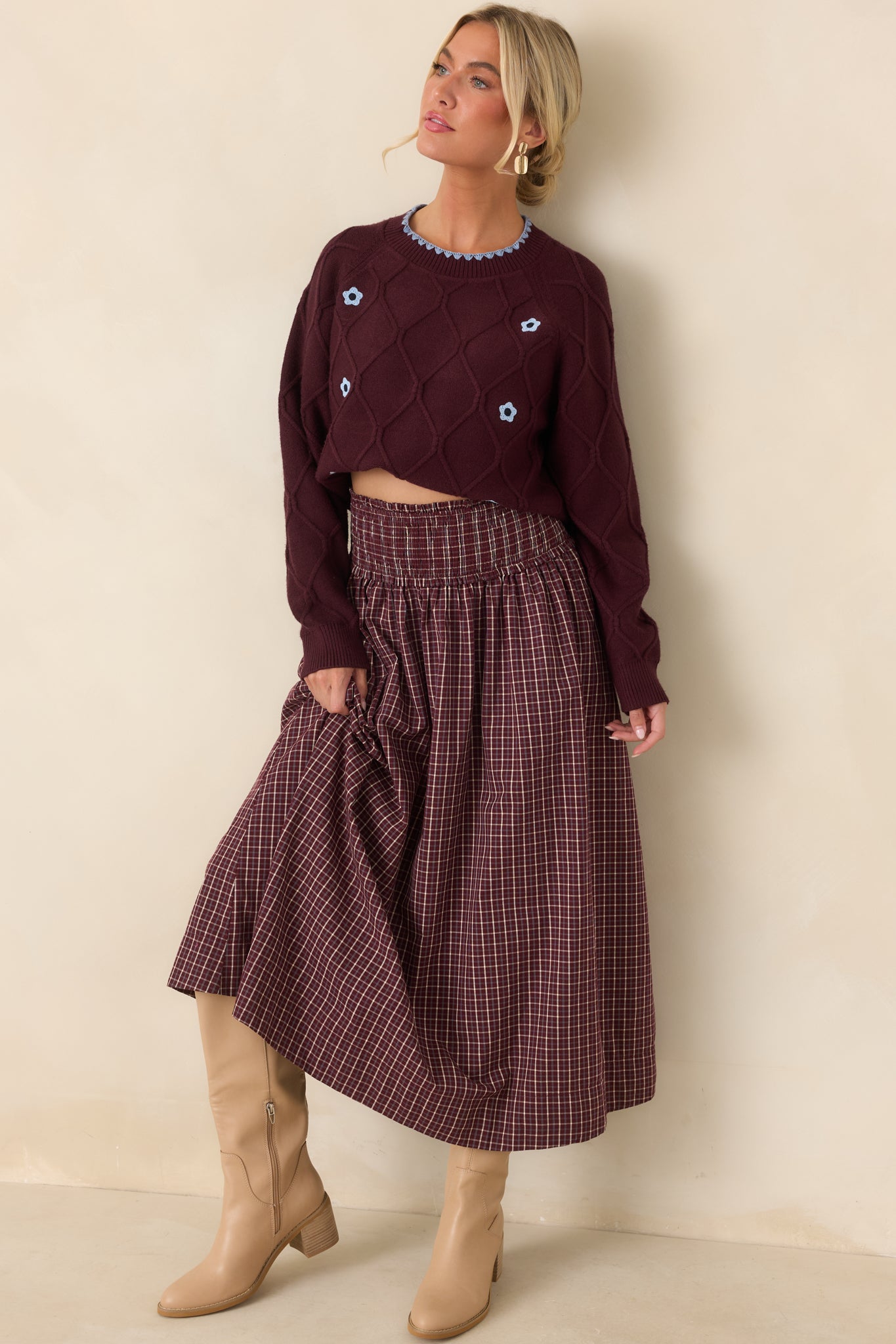 Burgundy diamond-knit sweater featuring light blue floral accents, scalloped crew neckline trim, long sleeves, ribbed cuffs, and a relaxed cropped silhouette.