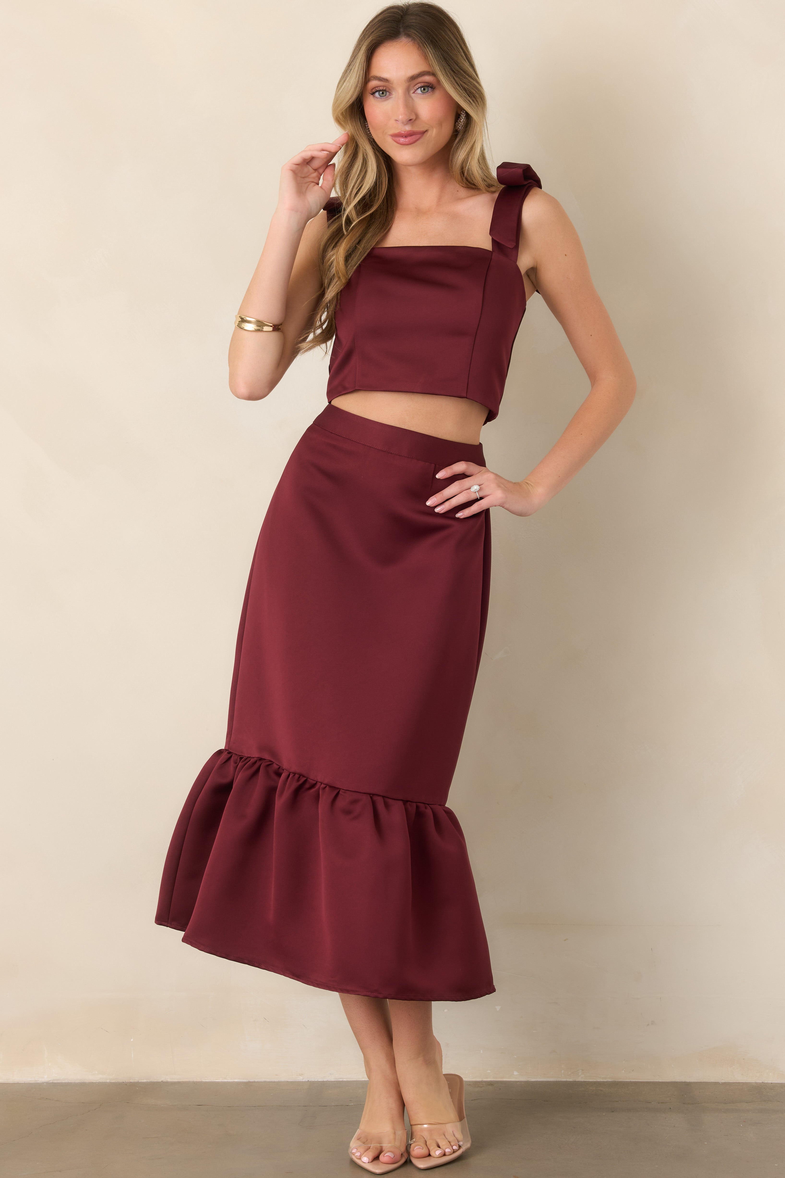 Rich burgundy midi skirt showcasing its sleek fitted shape, feminine length, and softly gathered flounce cascading along the hem.