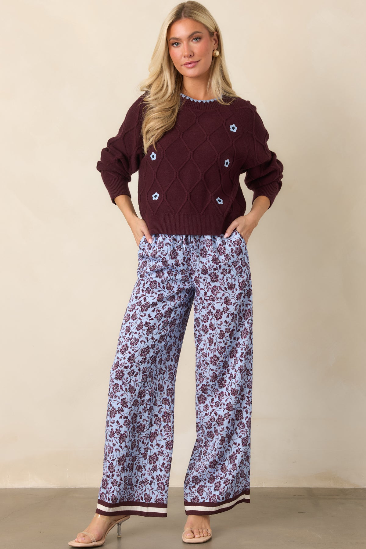 Burgundy floral pants on a pale lilac background with relaxed wide legs and contrasting striped hem detailing.