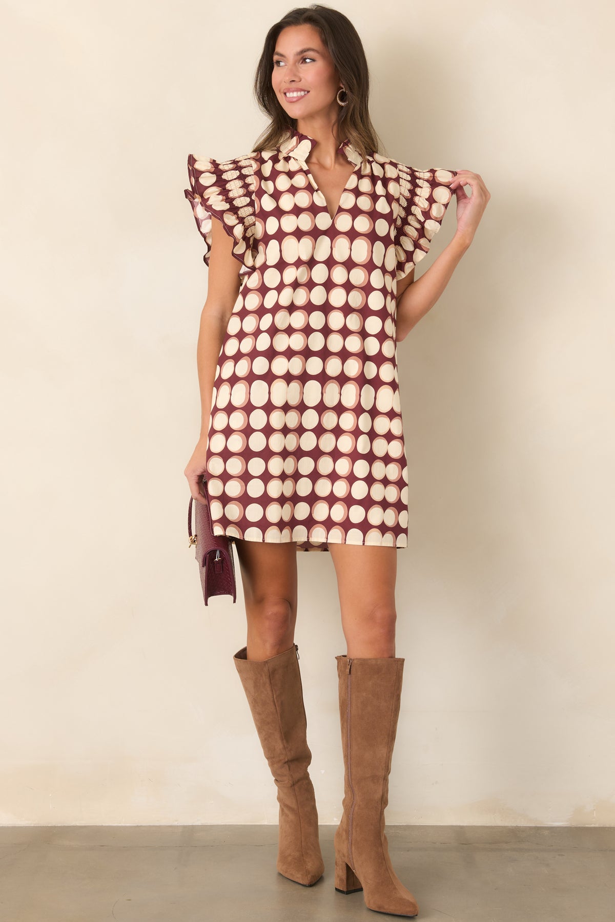 Loose burgundy mini dress with graphic ivory dots, a split neckline, gathered flutter sleeves, and ruffled sleeve edges.