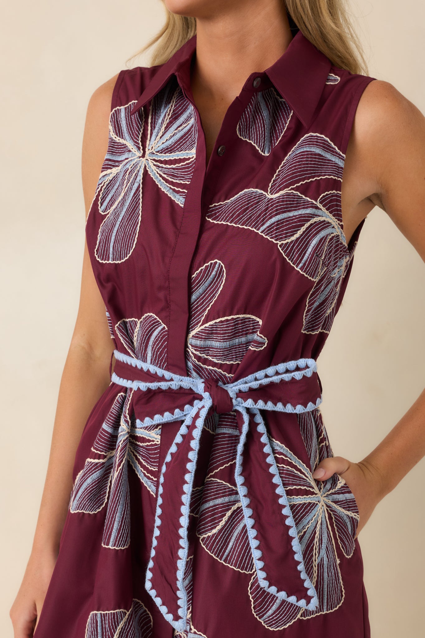 Close-up of the burgundy mini dress highlighting the embroidered floral motifs, hidden button-front closure, and blue scalloped trim accents.