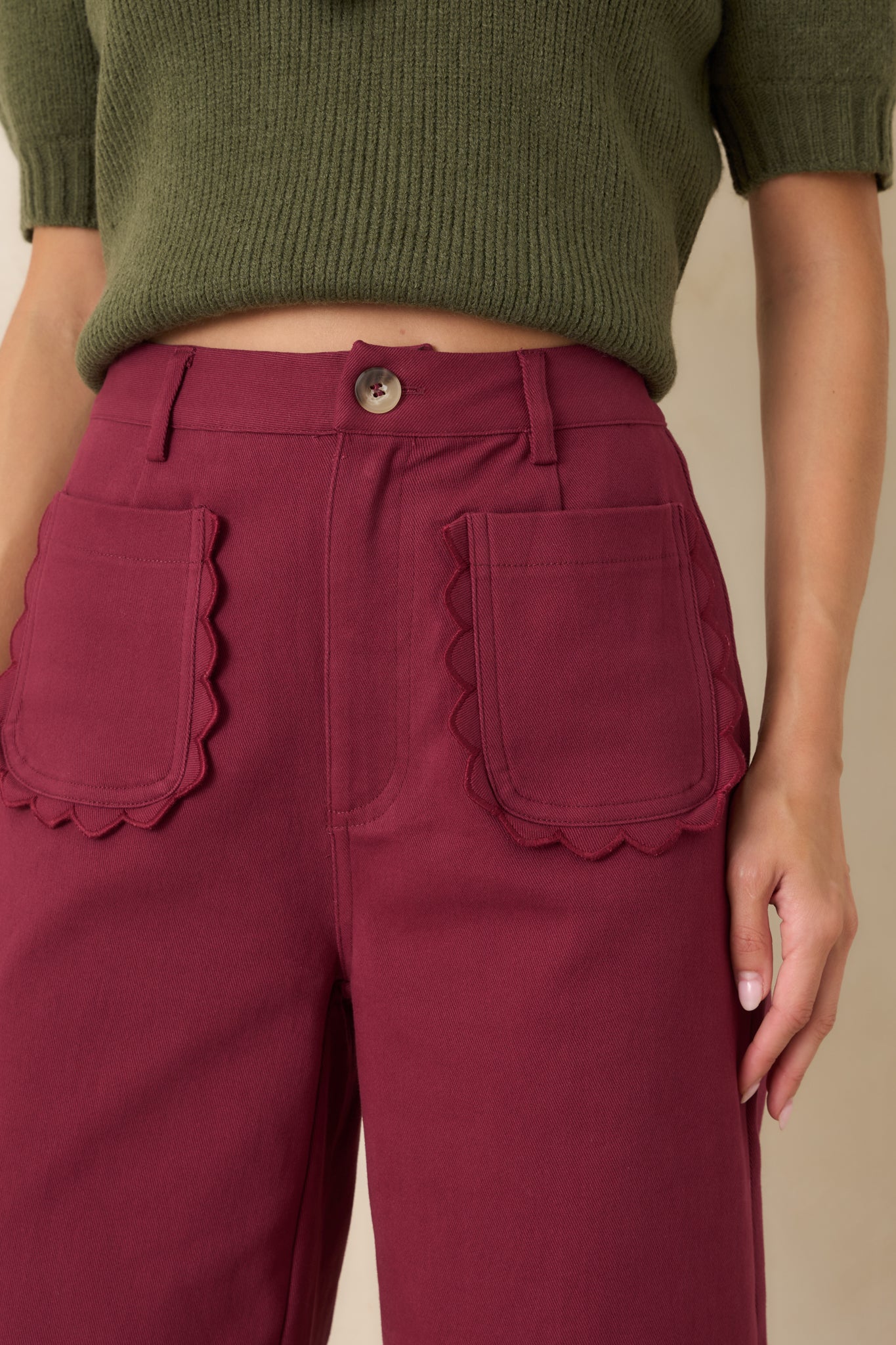 Close-up of the burgundy pants featuring the scalloped pocket edges, fabric texture, and polished front detailing.