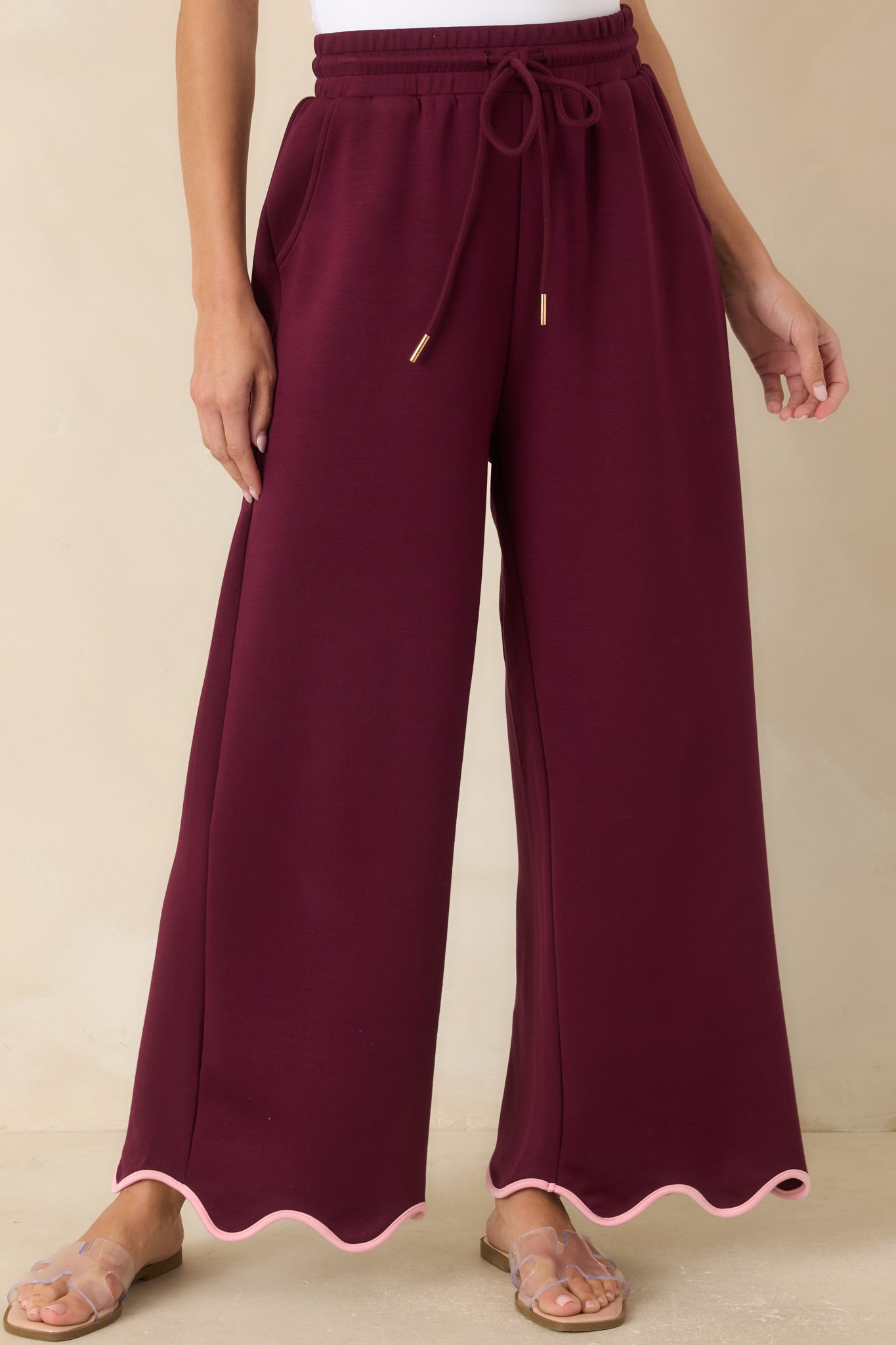 Burgundy pull-on pants featuring graceful wide legs and blush pink scalloped trim that adds subtle contrast at the hem.