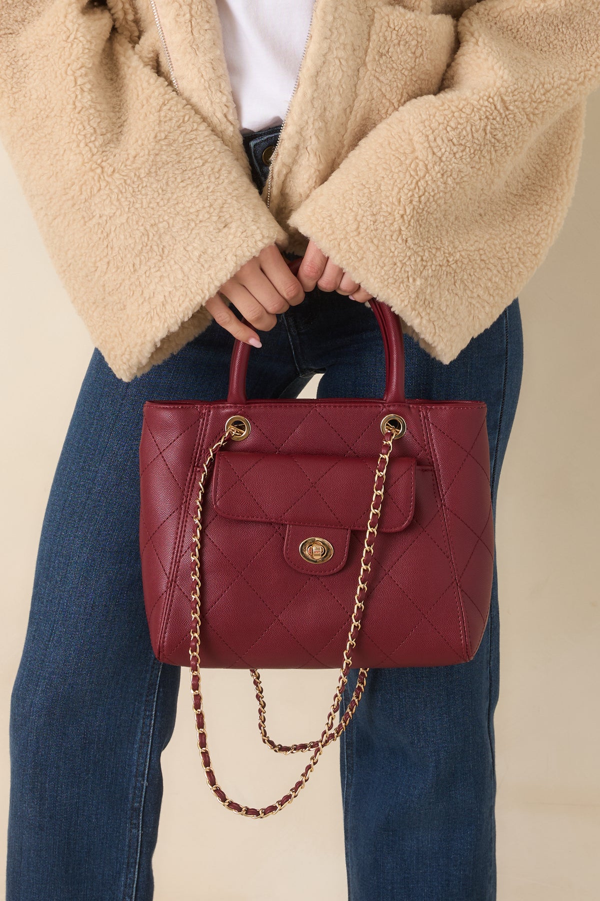 Burgundy quilted handbag with diamond stitching, rounded top handles, and gold-tone hardware.
