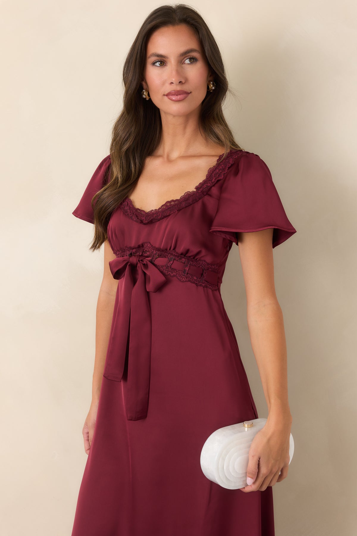 Burgundy satin dress featuring a front-tied ribbon bow, flutter sleeves, and a flowing midi skirt.