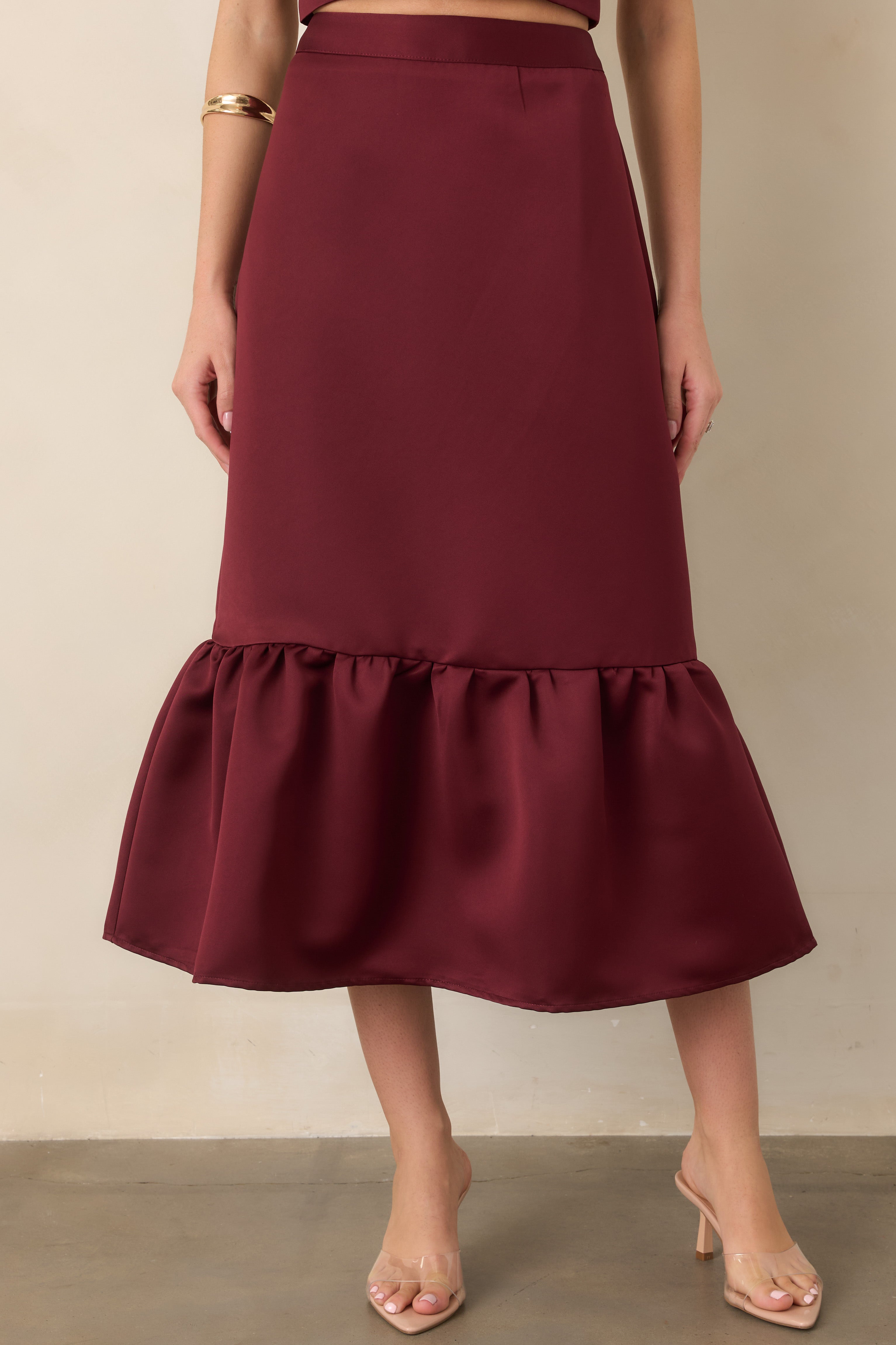 Close view of the burgundy satin skirt emphasizing its smooth sheen, fitted construction, and gently gathered flounce at the lower hem.
