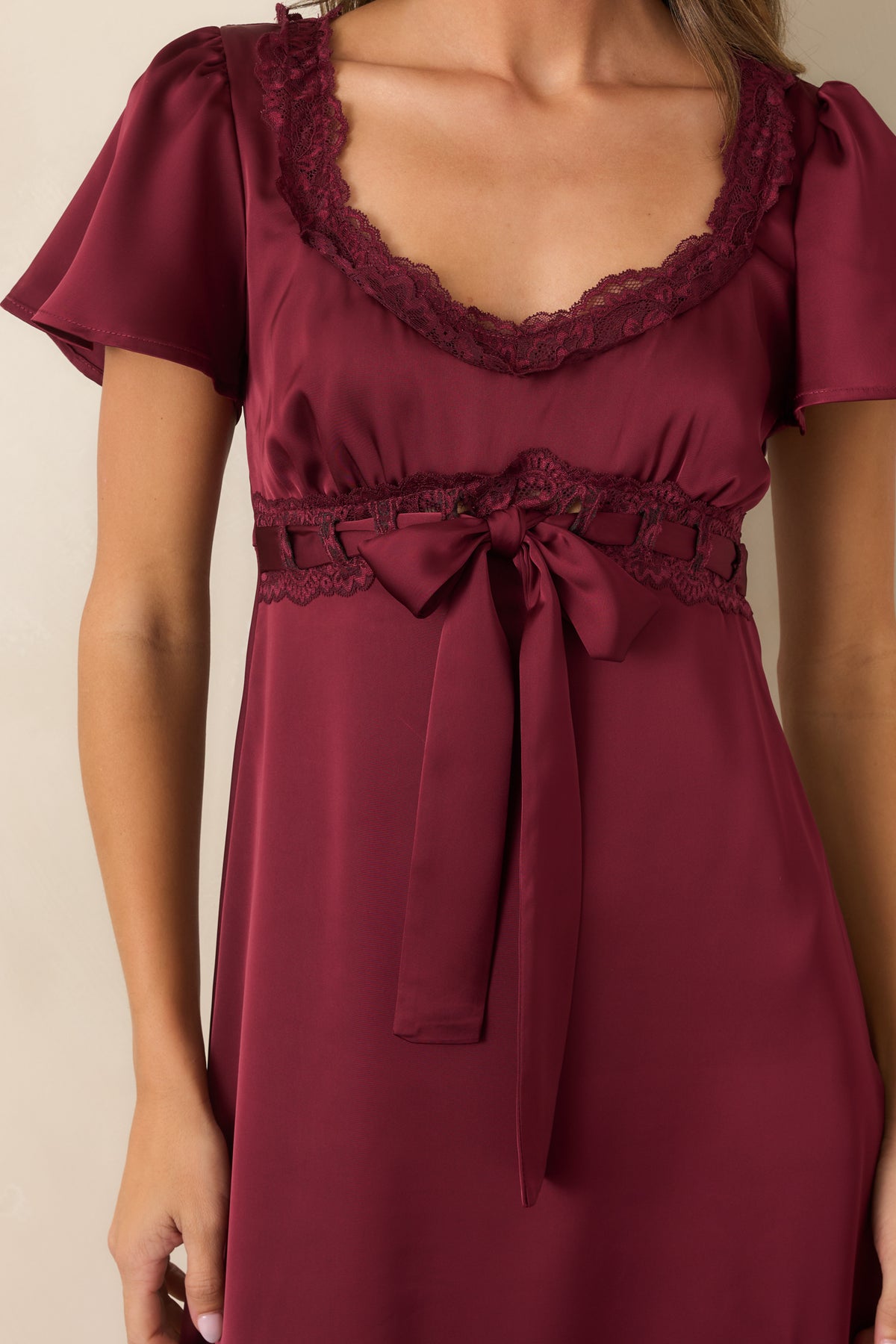 Close-up of the scalloped lace neckline, gathered burgundy satin bodice, and ribbon bow waist detailing.