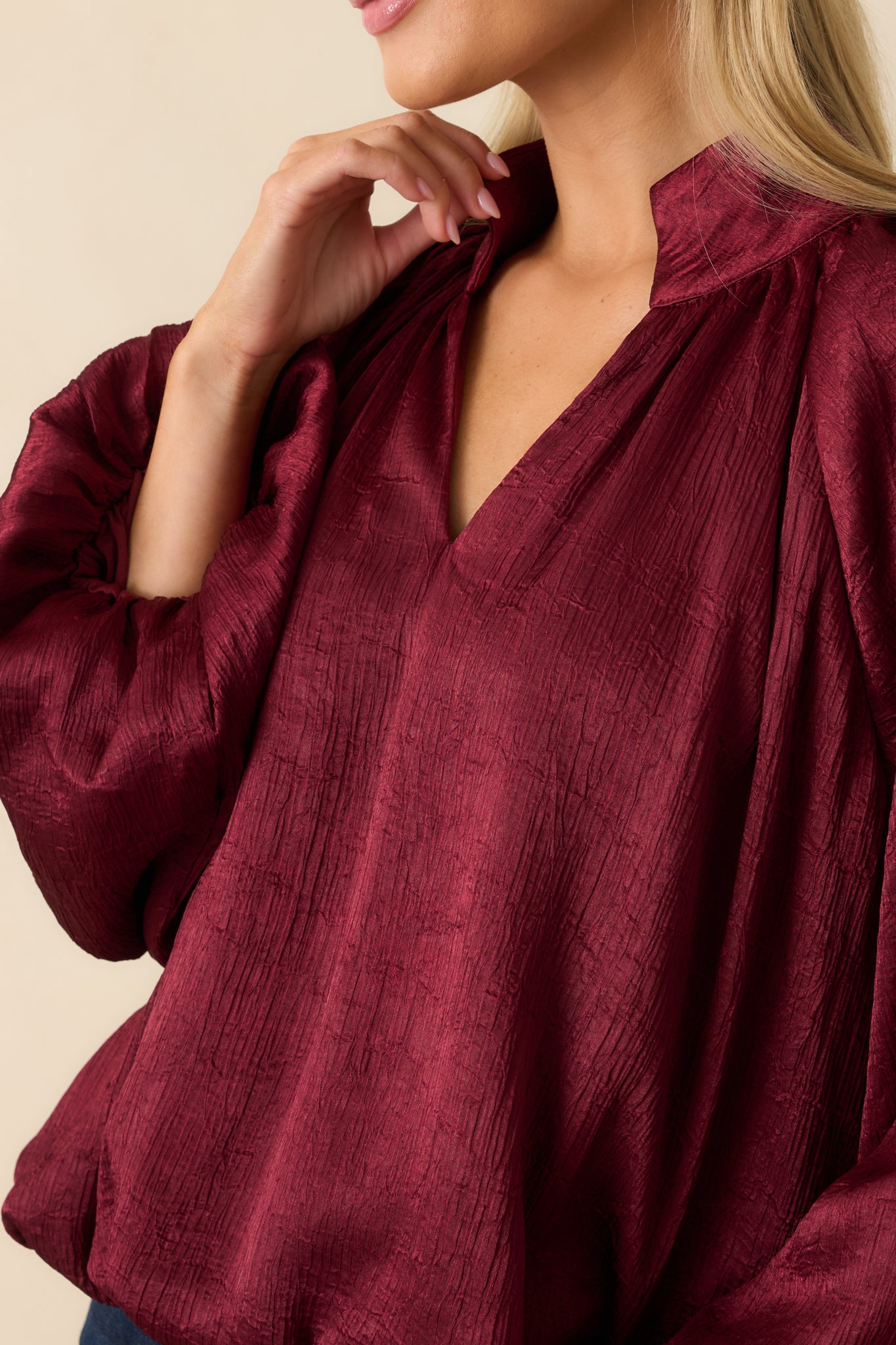 Detailed shot of the burgundy satin top showcasing the ruched neckline, gathered sleeve cuffs, and soft textured fabric.