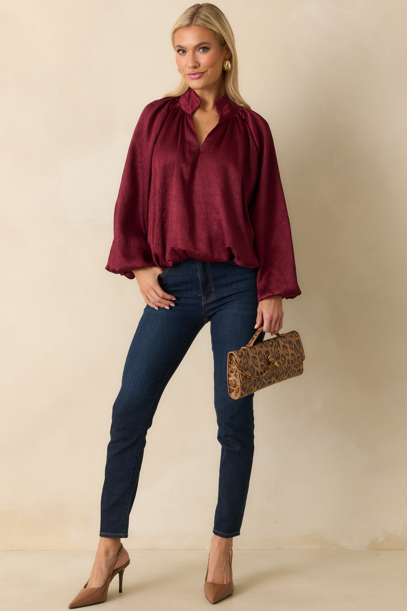 Elegant burgundy satin top with long sleeves, gathered cuffs, and a softly ruched neckline for gentle shaping.