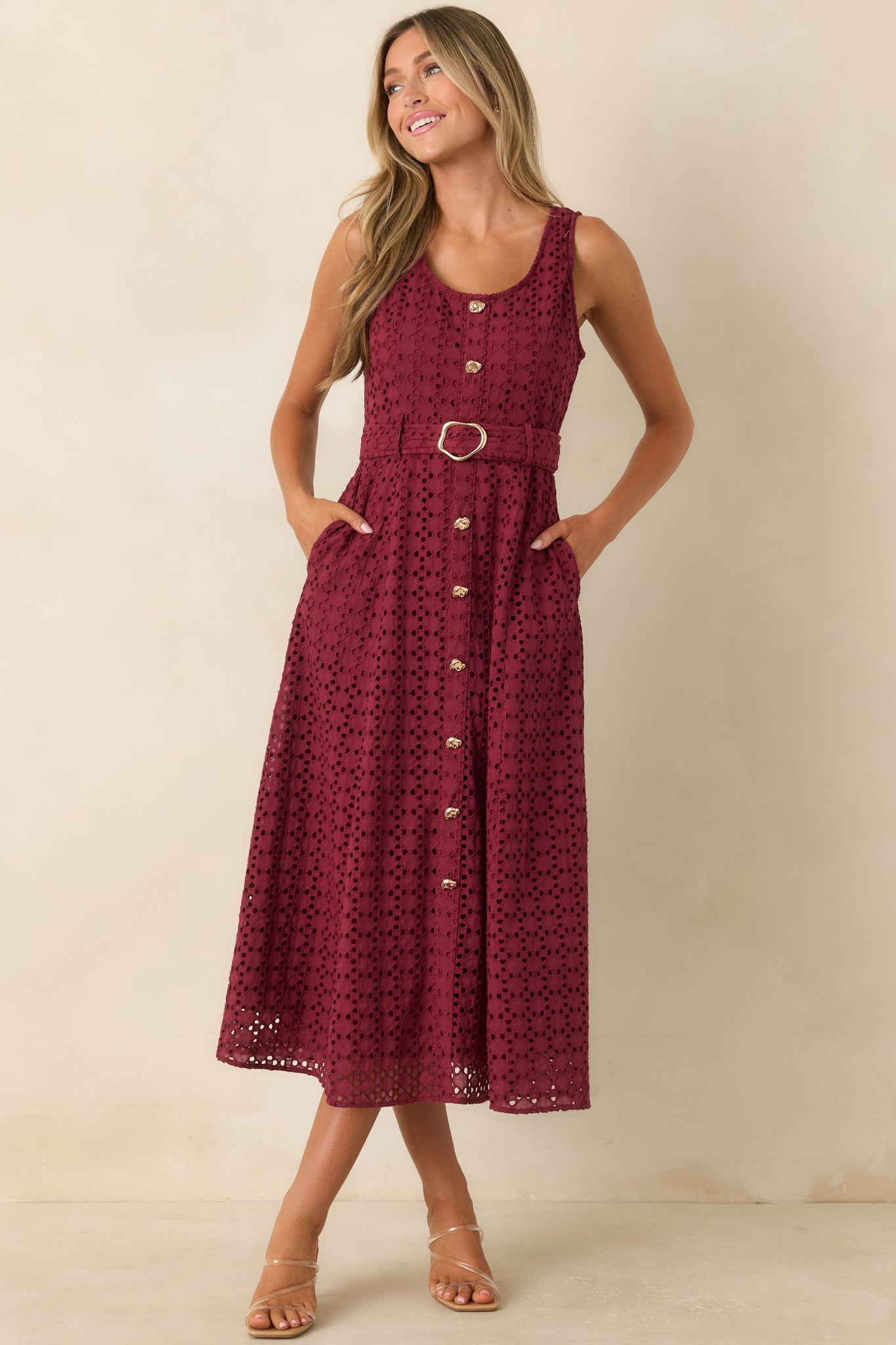 Burgundy sleeveless midi dress designed with full eyelet embroidery, a faux button front, removable belt, and flowing silhouette.