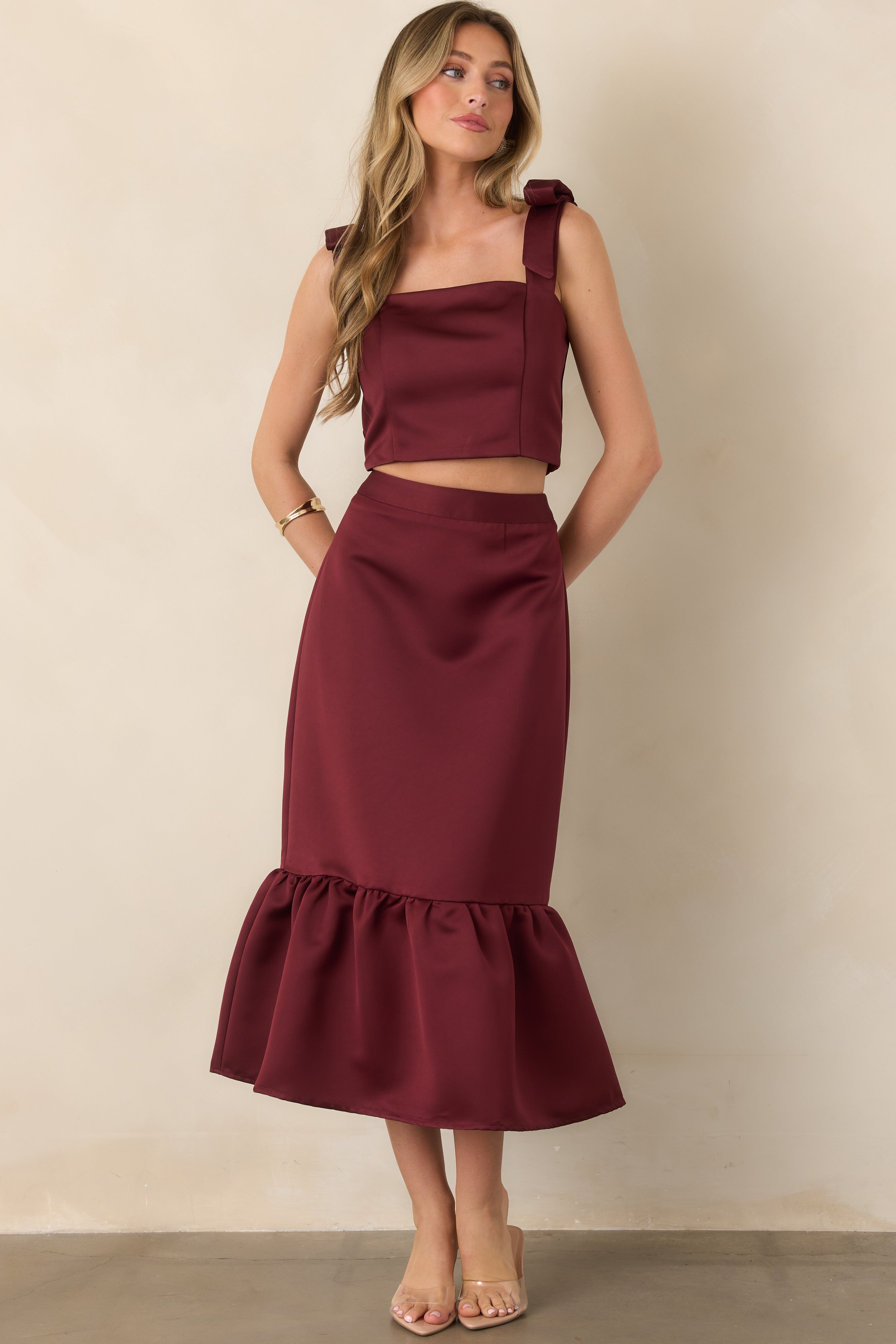 Feminine satin top highlighting the structured square neckline, sculpted cropped shape, and decorative shoulder bows in a deep burgundy hue.