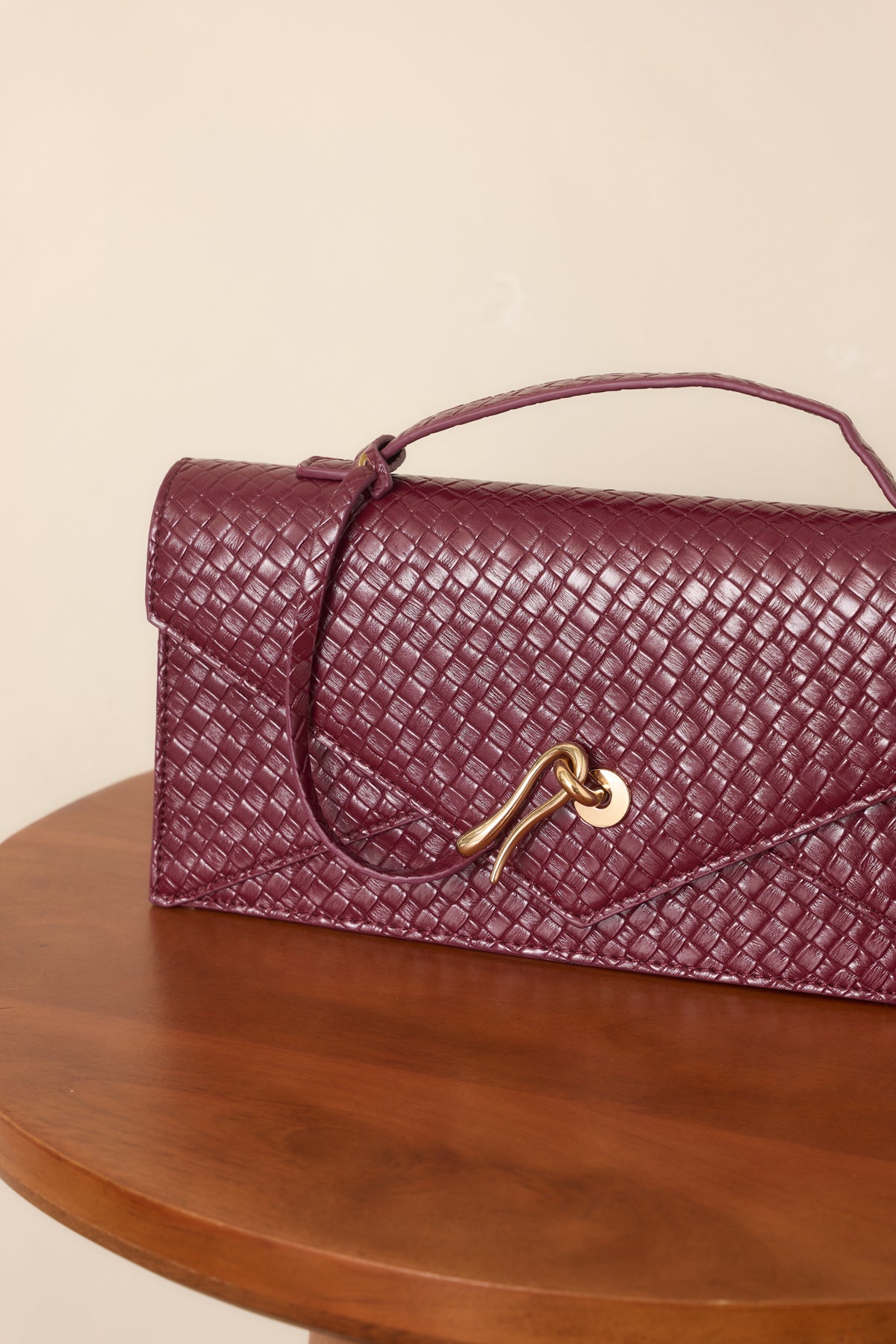 Burgundy clutch highlighting the textured woven faux leather and sculptural gold-tone hardware.