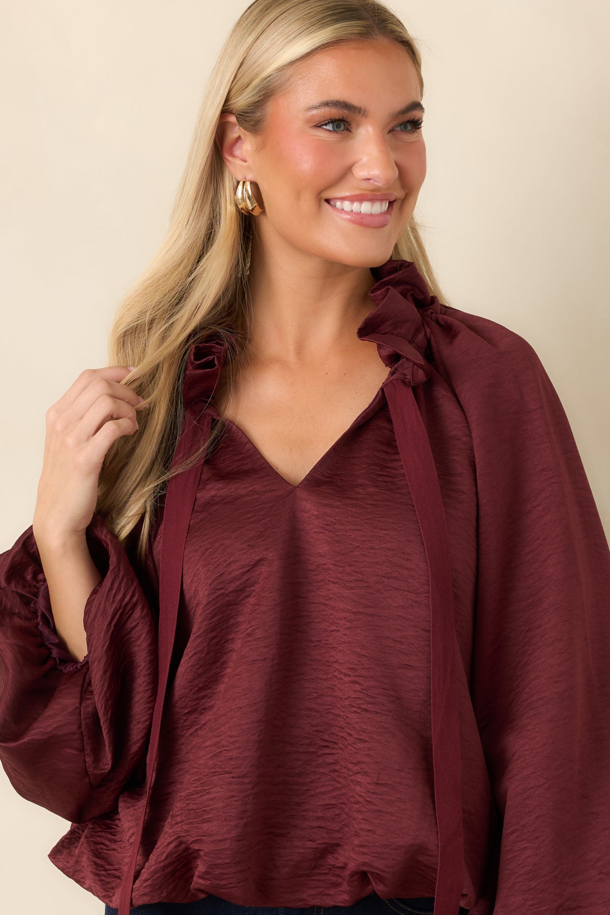 Ruffled stand collar frames the split V-neckline of the burgundy top, finished with long adjustable ties.