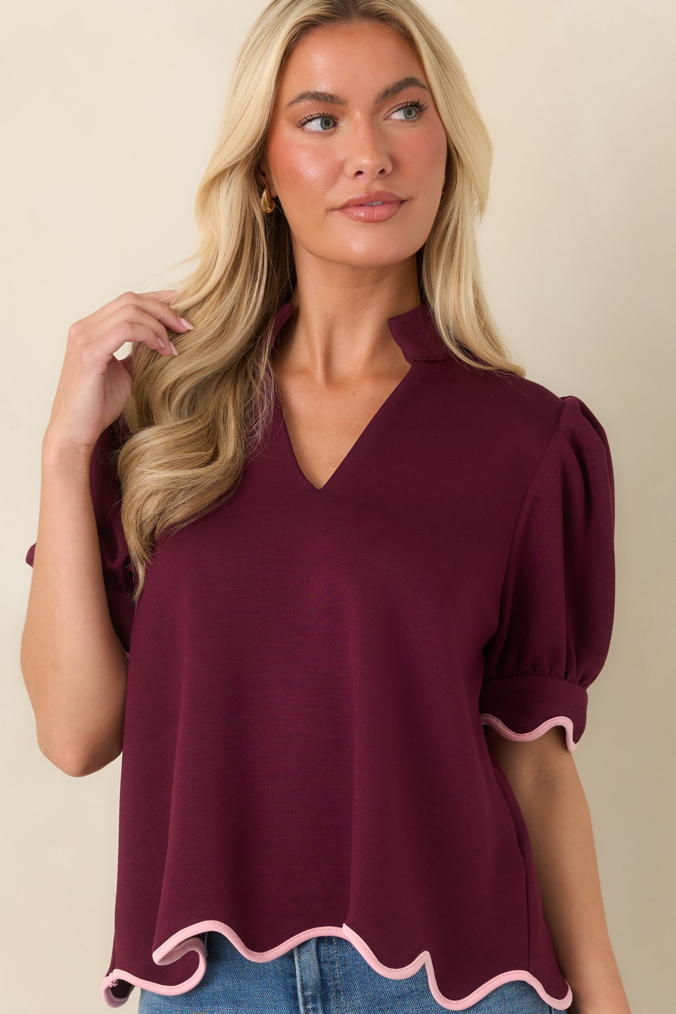 Close view of the burgundy top emphasizing its soft knit texture, puff sleeves, and decorative scalloped edging.