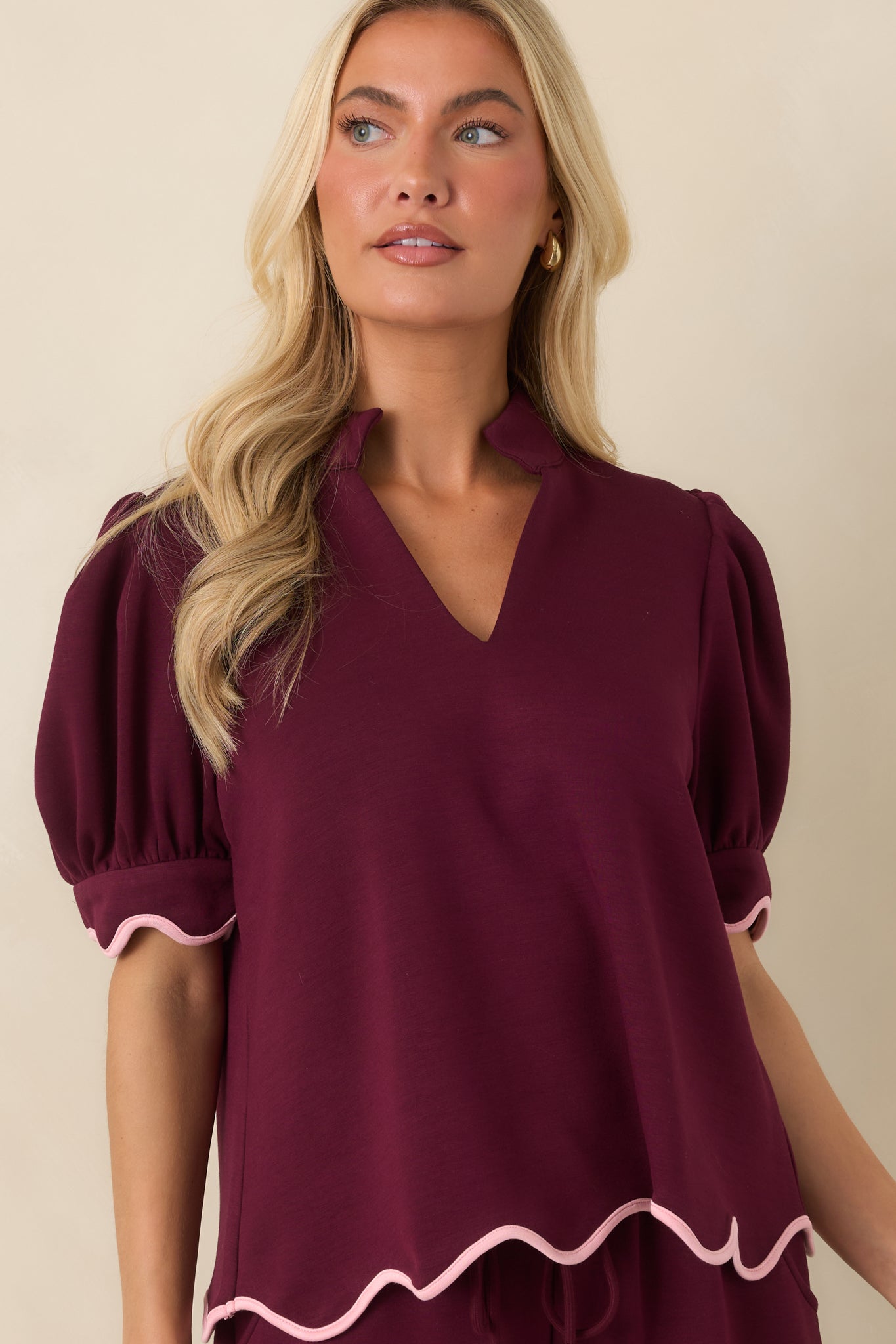 Burgundy knit top highlighting the split neckline and stand collar paired with contrasting blush pink scalloped details.