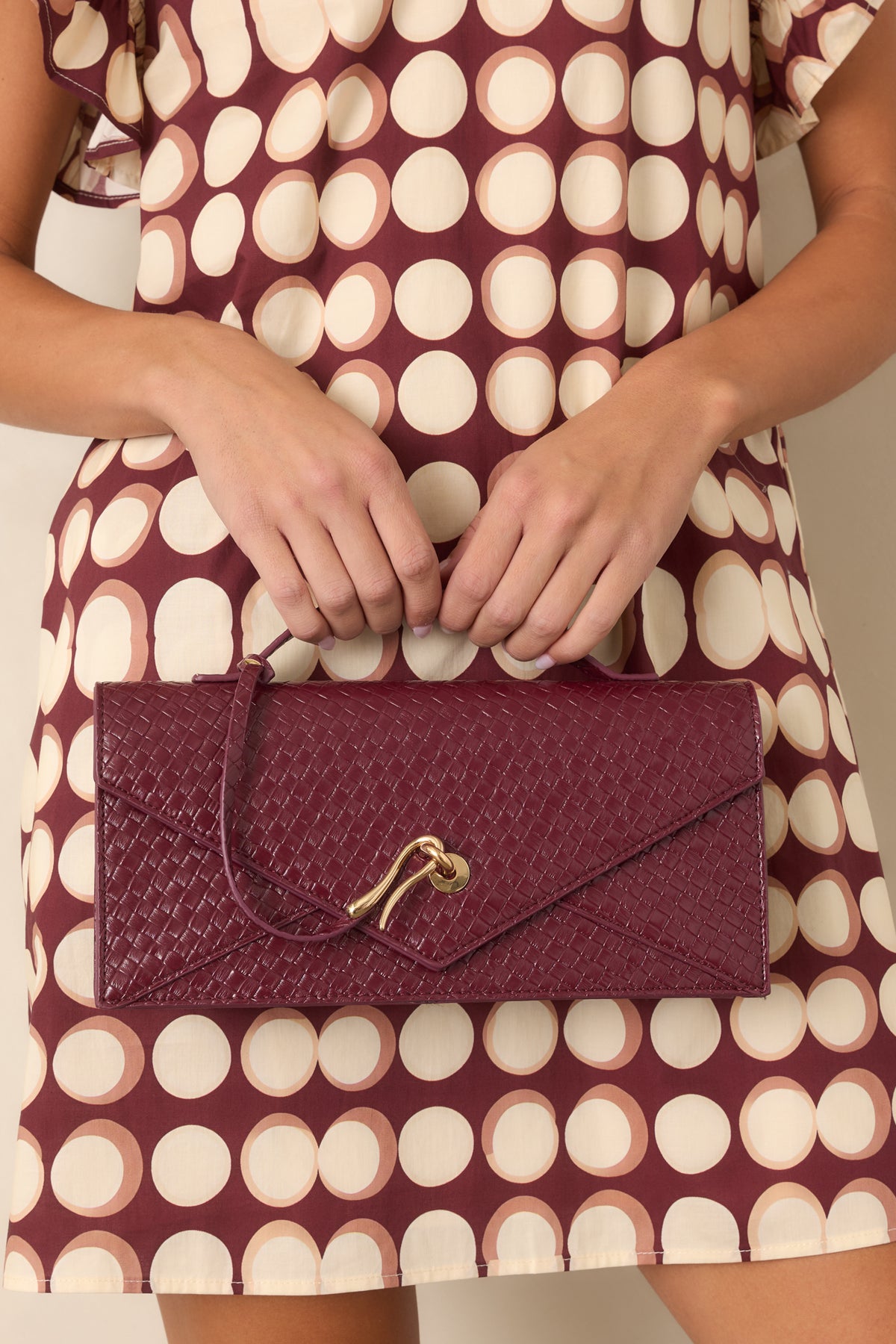 Burgundy woven clutch highlighting the textured faux leather and structured envelope shape.