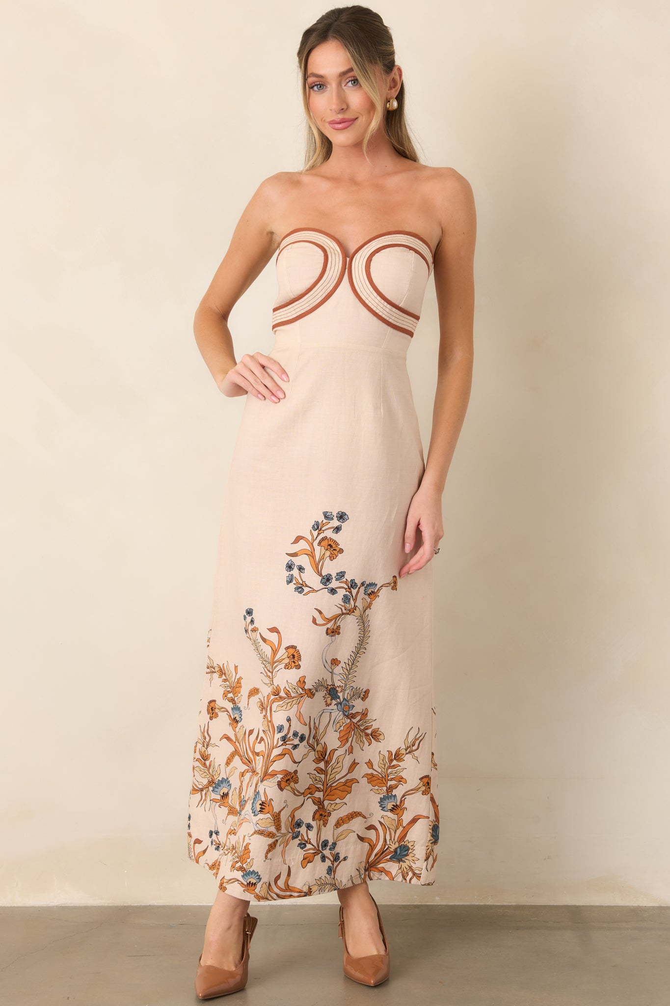 Long column-style dress combining a shaped strapless bodice, fitted waist, and colorful floral detailing in burnt orange and muted blue.