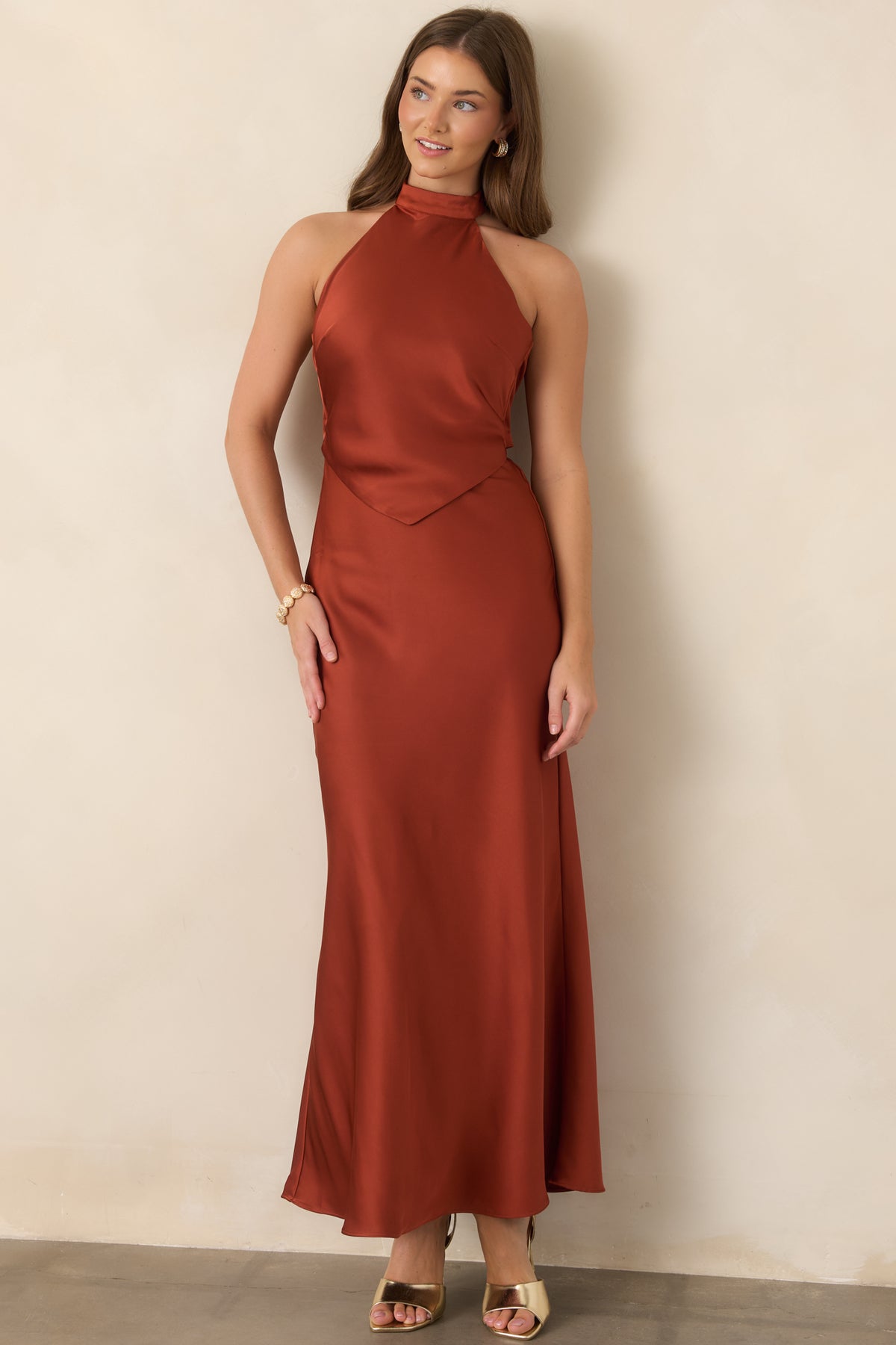 Burnt sienna satin maxi dress showcasing a sleek halter neckline, pointed bodice overlay, and fluid floor-length skirt with graceful movement.