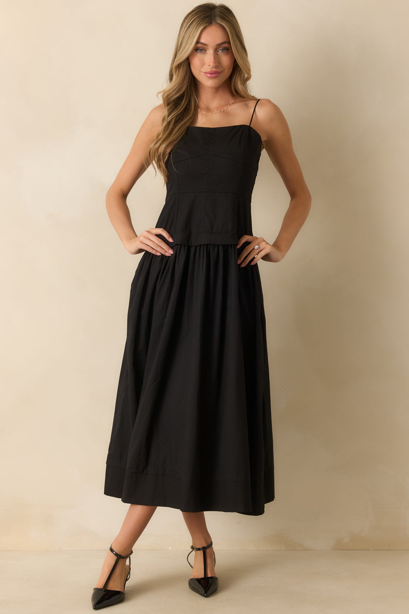 Bustier-style black midi dress with adjustable straps, a fitted top, and a softly gathered skirt.