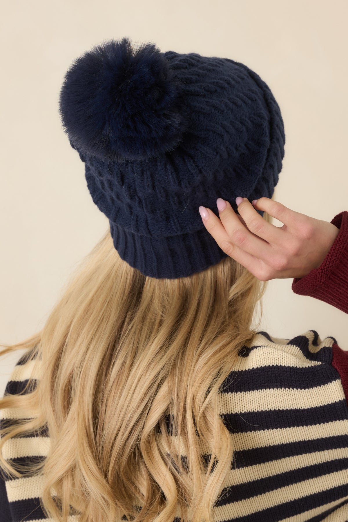 Rear view of the cable-knit hat showcases its textured stitching, relaxed crown, and wide fold-over ribbed cuff.