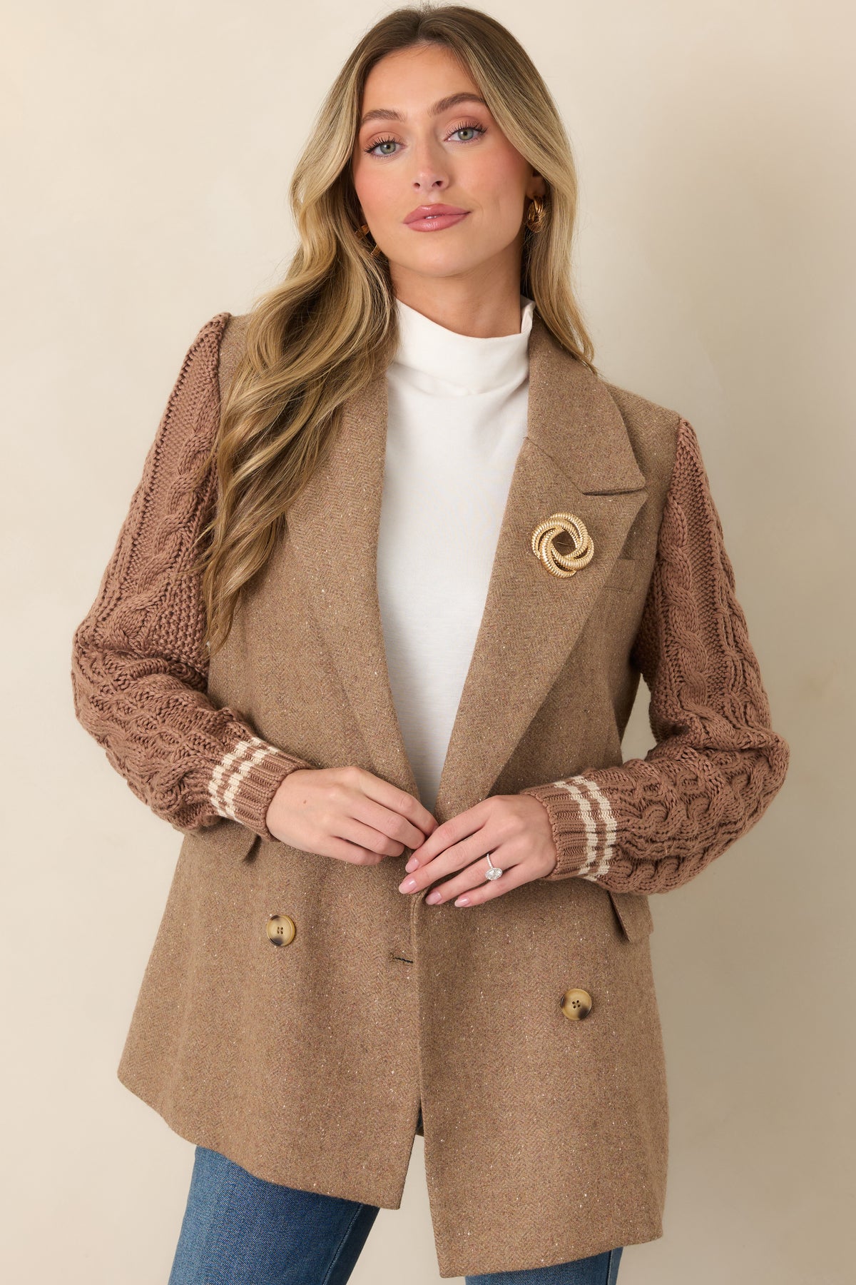 Close view of the front flap pocket and textured cable-knit sleeve against the smooth camel wool-blend body.