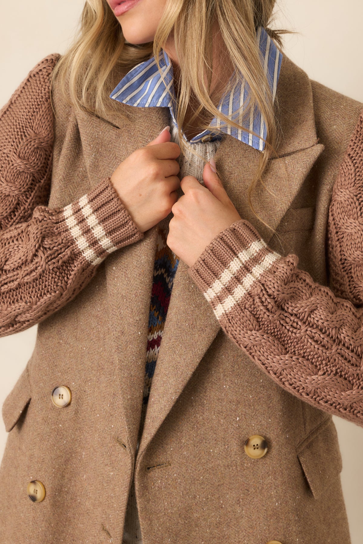 Close view of the camel blazer's notched lapels, button closures, flap pocket, and contrasting cable-knit sleeve texture.