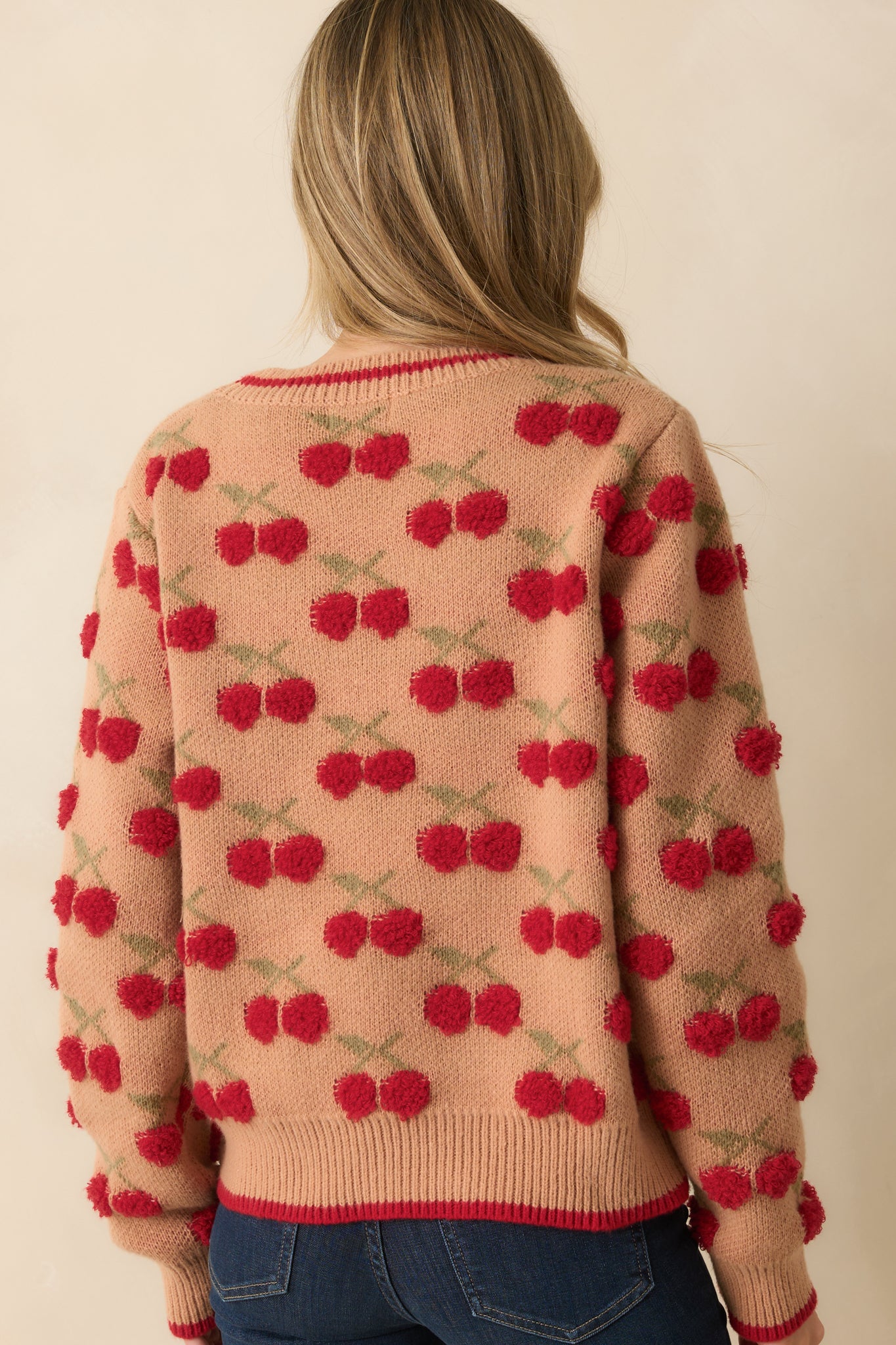 Rear view of the camel brown sweater showing long sleeves, ribbed hem, and cherry motif pattern.