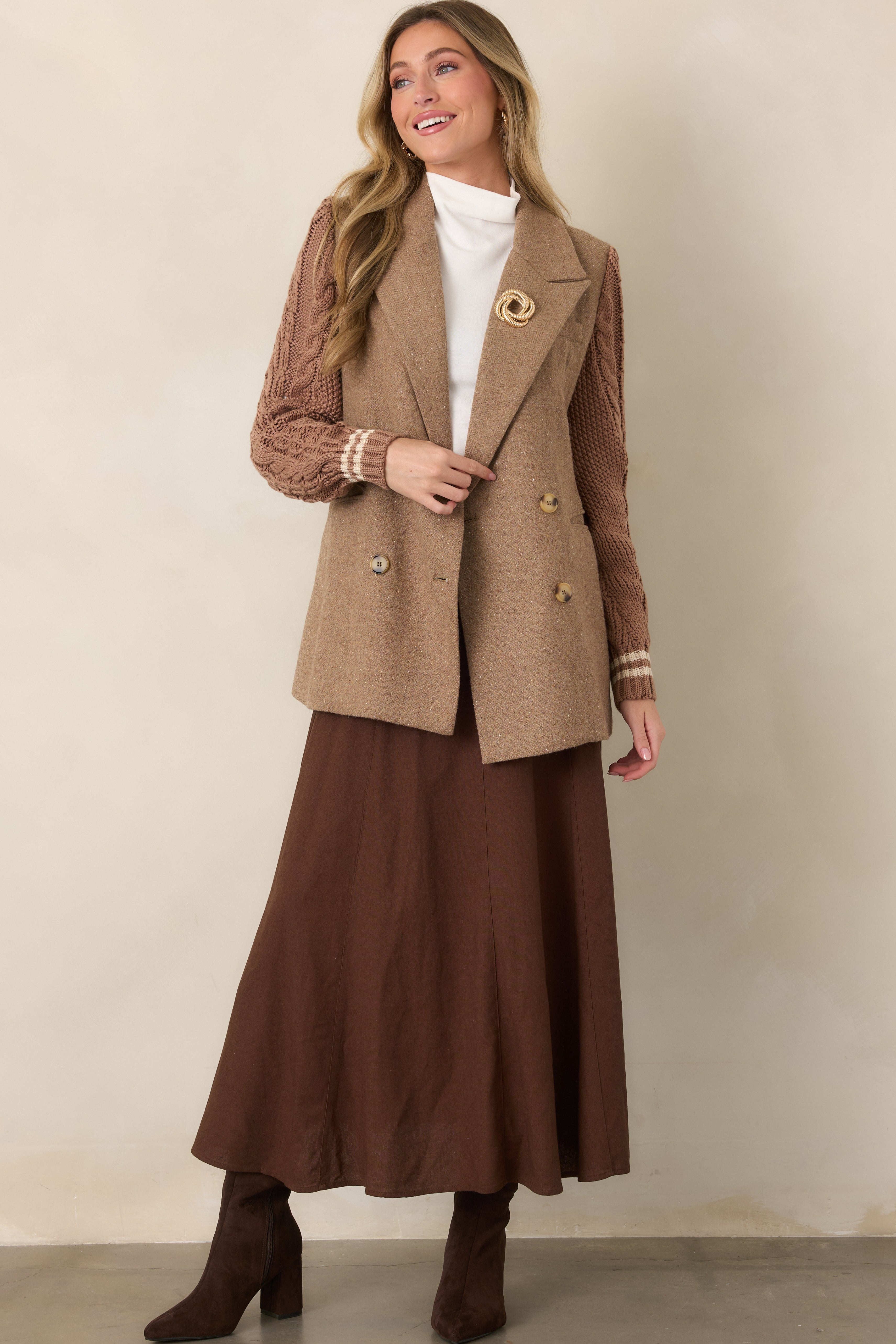 Mid-thigh camel blazer featuring button closures, tailored lapels, front flap pockets, and cable-knit sleeves with ribbed cuffs.