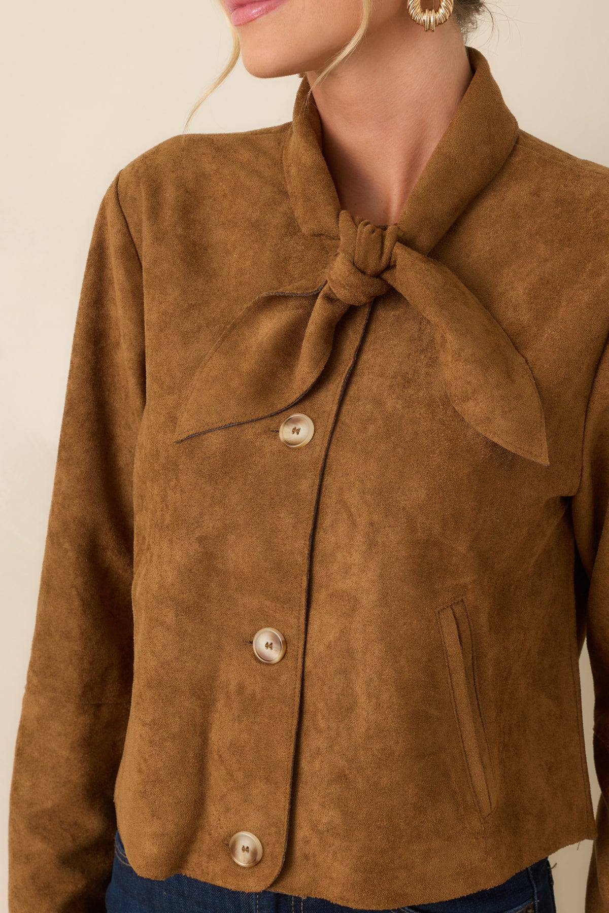 Close-up of the camel faux suede jacket highlighting its soft texture, neckline tie, polished buttons, and refined stitching.
